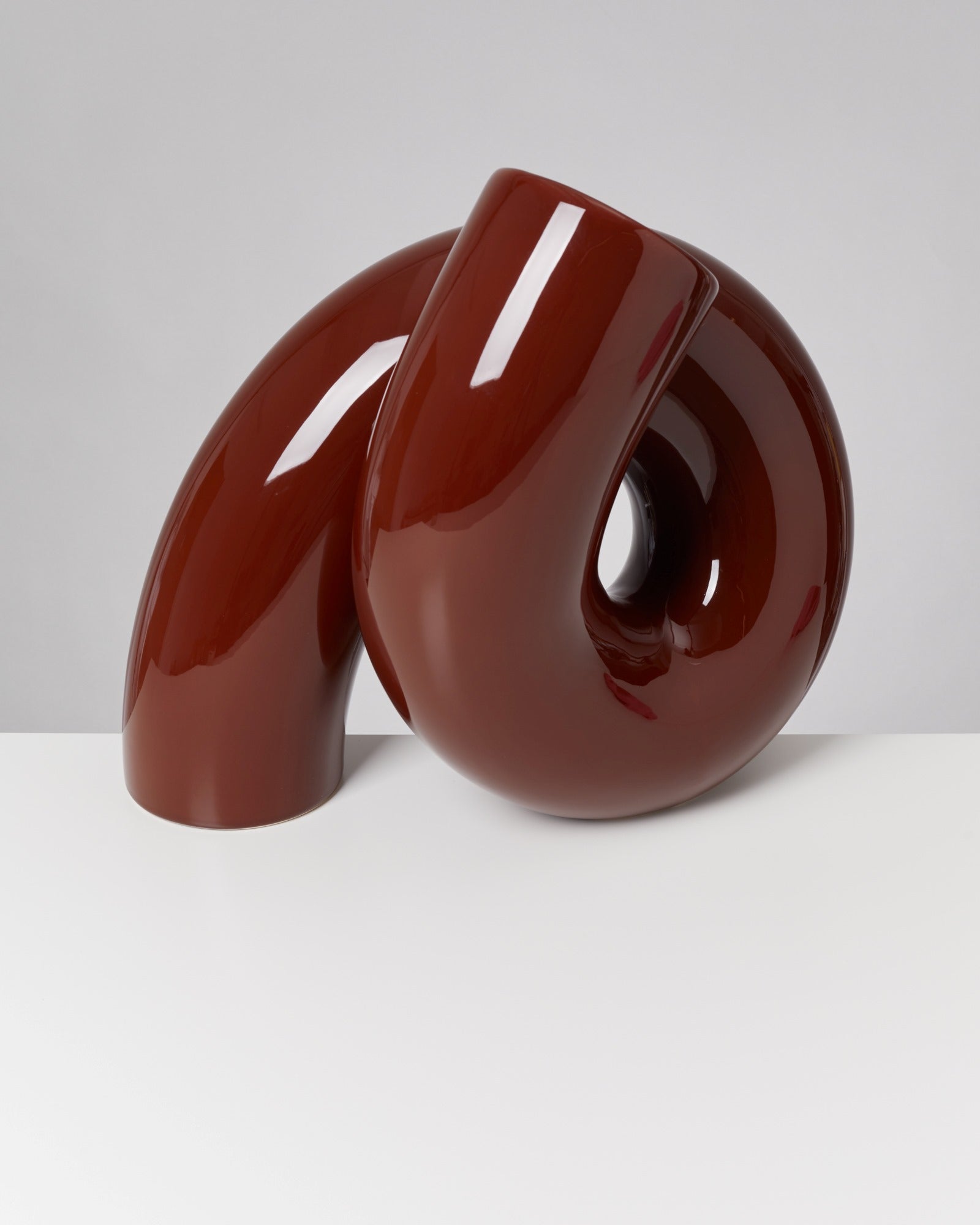 Rote, glänzende, abstrakte Skulptur in geschwungener Form auf weißem Hintergrund.