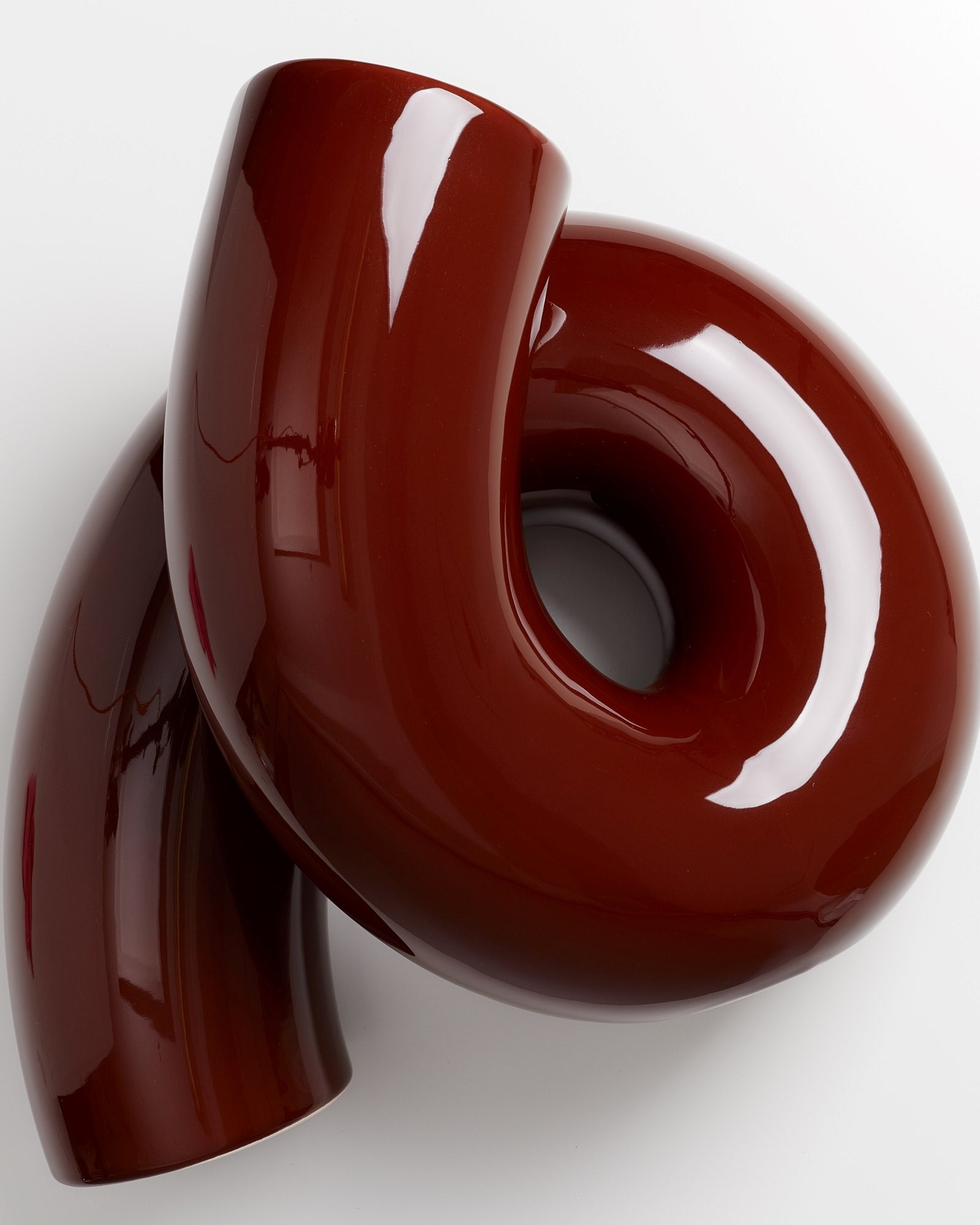 Rote, glänzende Kunststoffskulptur mit verschlungenen, röhrenförmigen Elementen auf weißem Hintergrund.