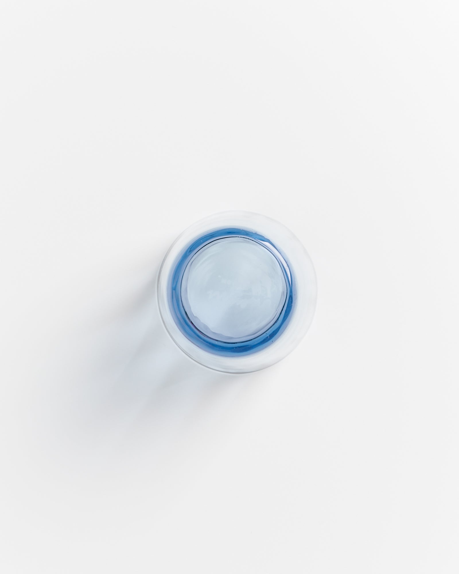 Ein Glas mit blauem Inhalt steht auf einer weißen Oberfläche, von oben betrachtet.