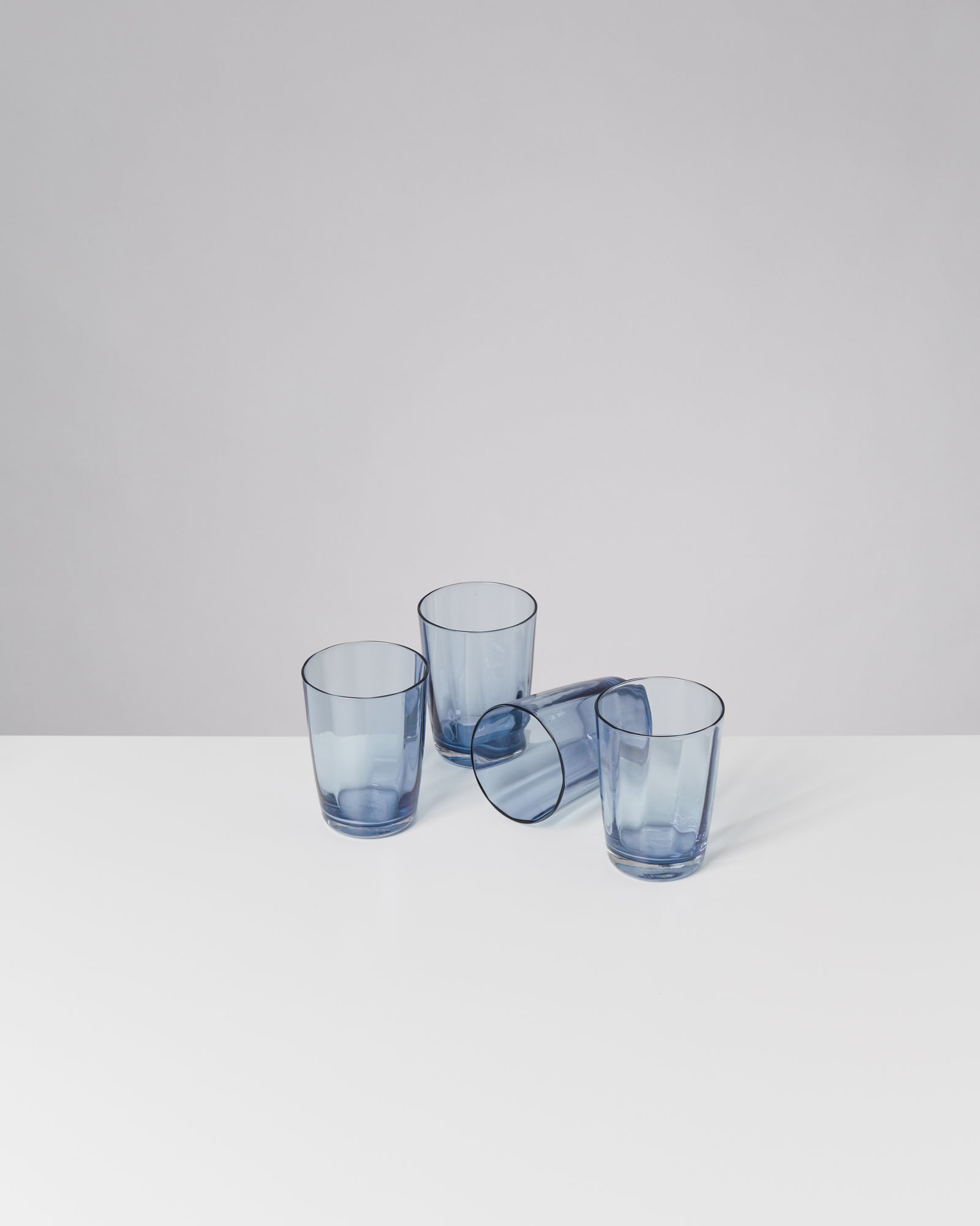 Vier blaue Gläser stehen auf einem weißen Tisch, eines davon liegt umgekippt.