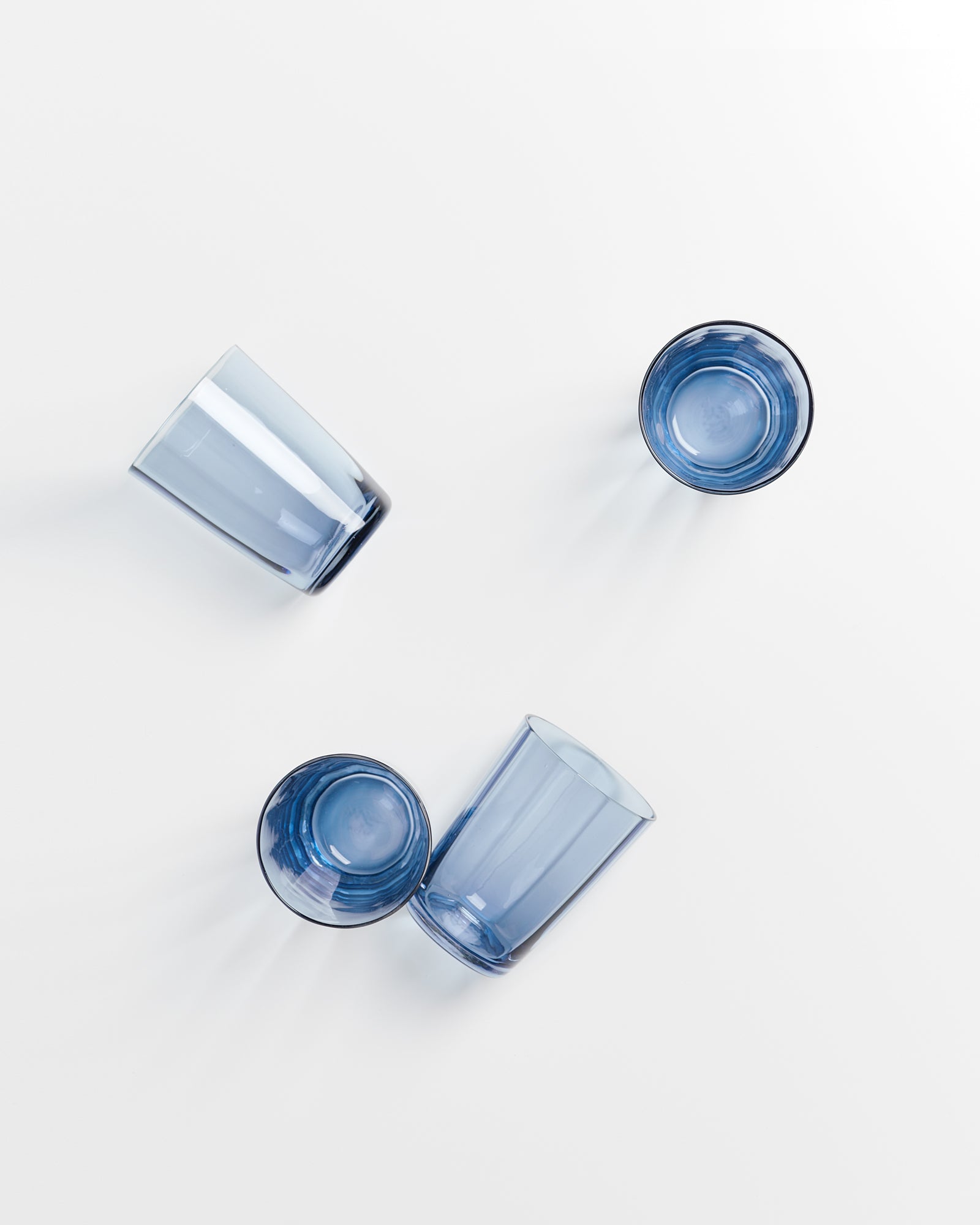 Vier blaue Trinkgläser liegen und stehen verstreut auf einer weißen Oberfläche.