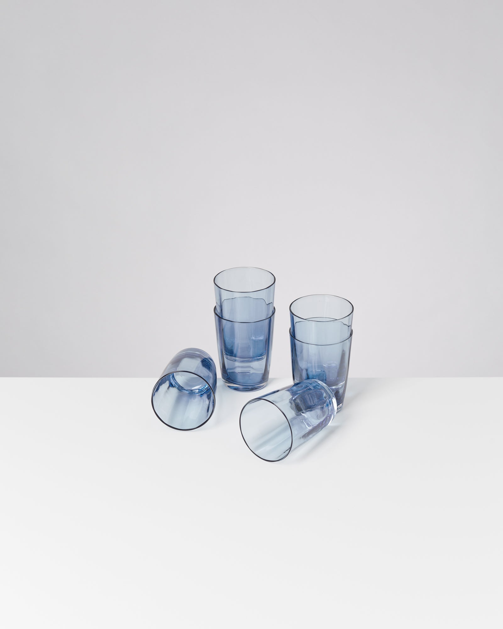 Vier blaue Glasbecher, zwei stehen aufrecht, zwei liegen auf der Seite auf einem weißen Tisch.