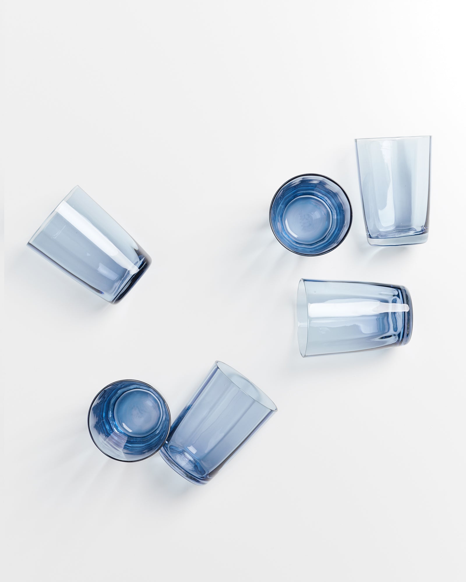 Sechs blaue Gläser liegen verstreut auf weißem Hintergrund.