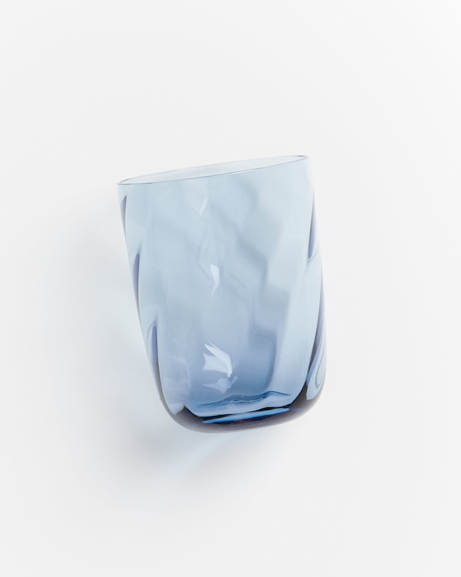 Bläuliches Glas mit schrägem Boden, schimmerndem Finish und wellenartiger Oberfläche vor weißem Hintergrund.