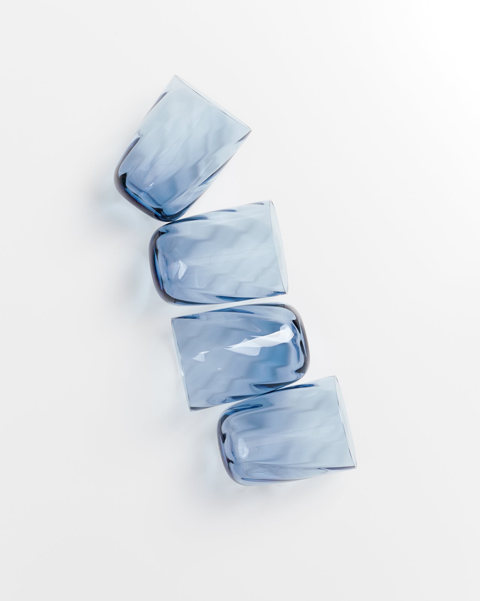 Vier blaue, durchsichtige Gläser liegen schräg nebeneinander auf weißem Hintergrund.