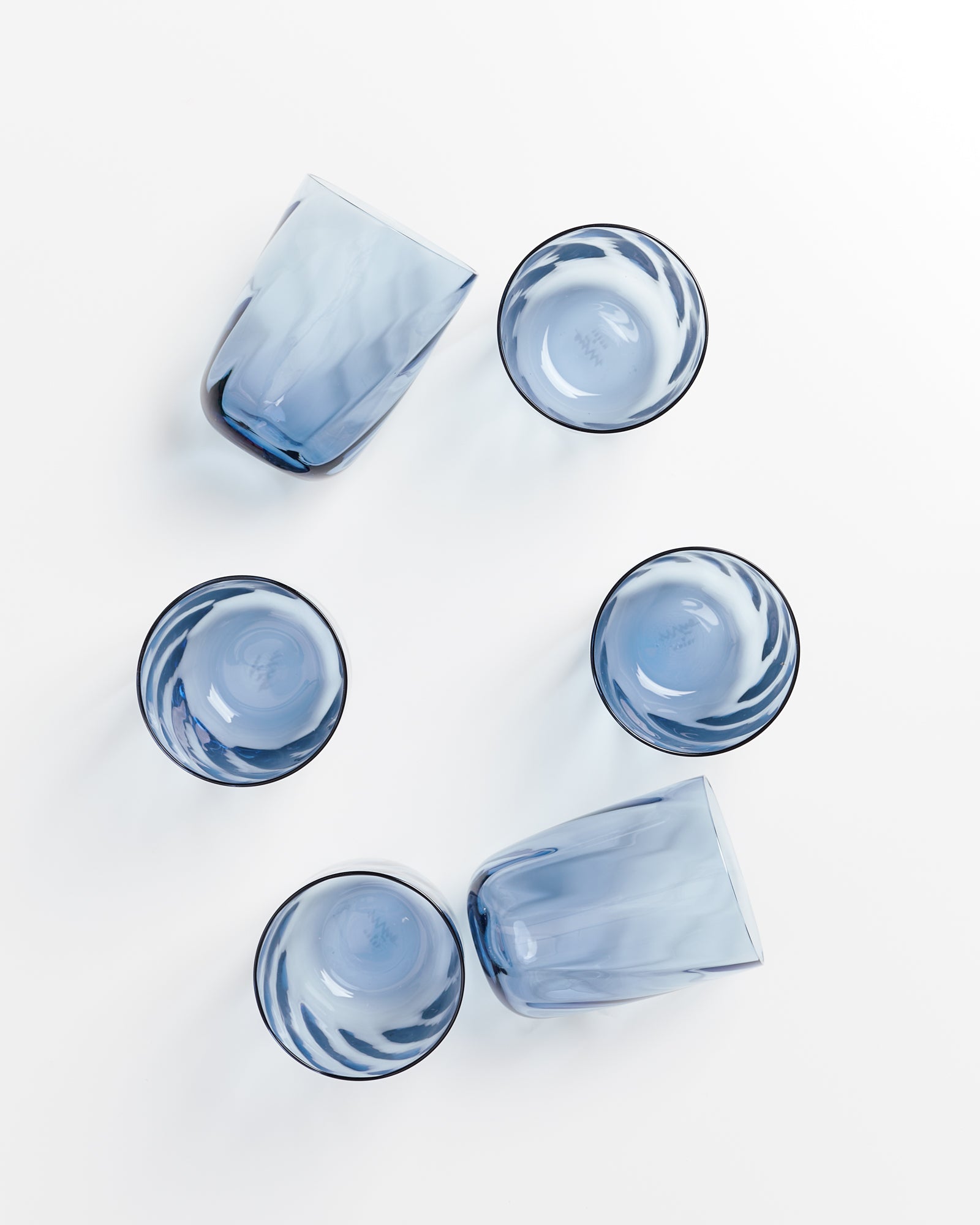 Sechs blaue Gläser, aus verschiedenen Winkeln fotografiert, liegen auf einer weißen Oberfläche.