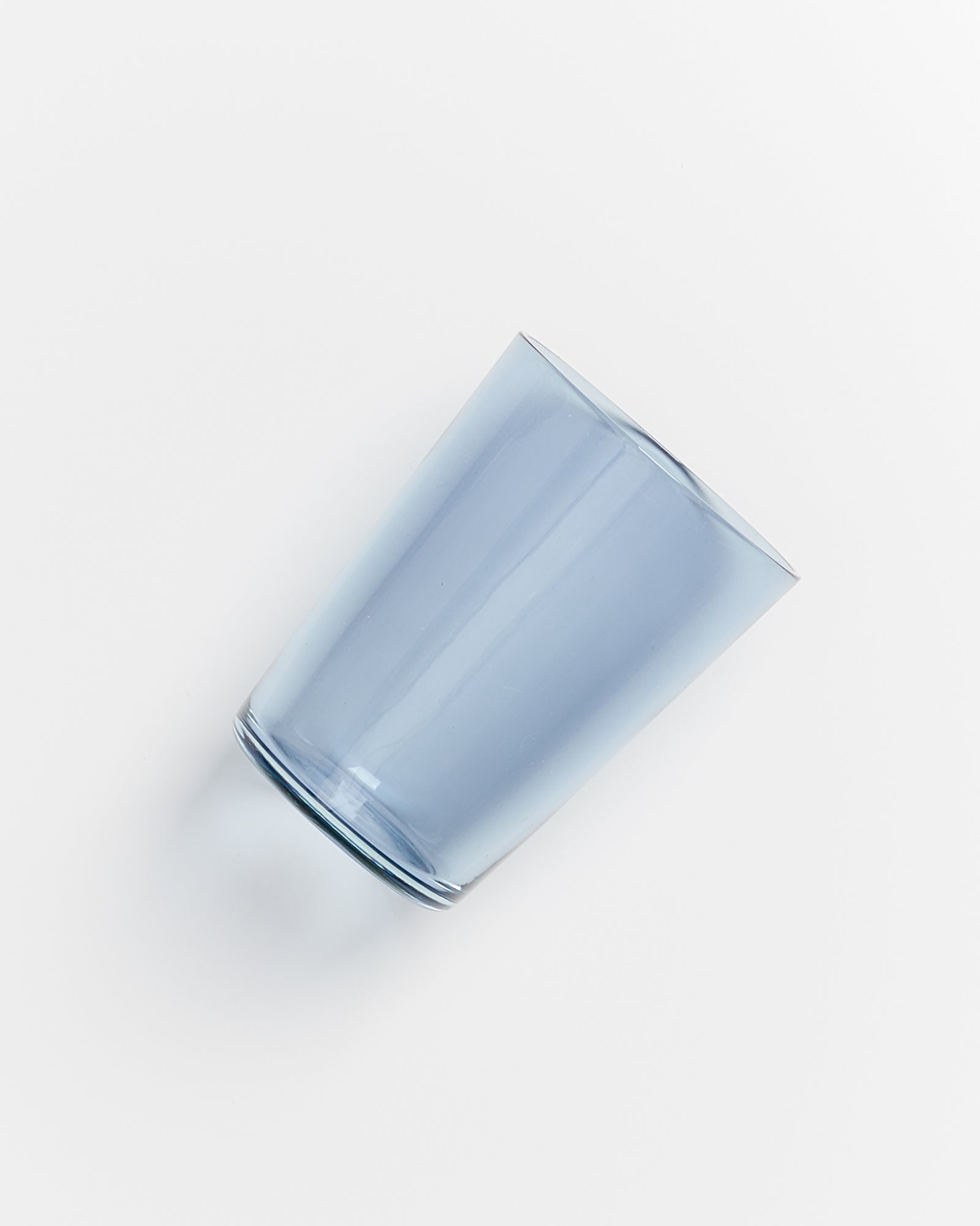 Ein blaues, transparentes Trinkglas liegt auf einer weißen Oberfläche.