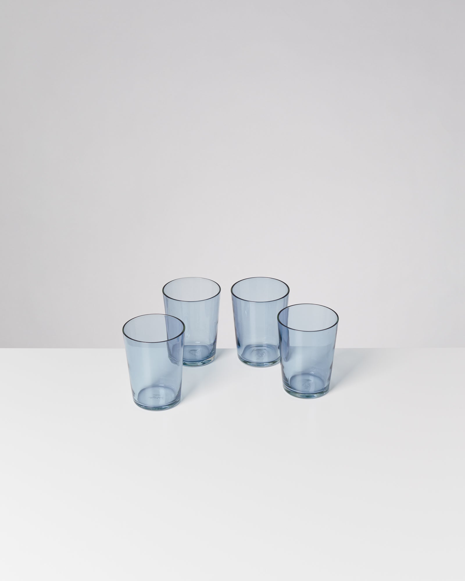 Vier blaue Trinkgläser stehen auf einem weißen Tisch.