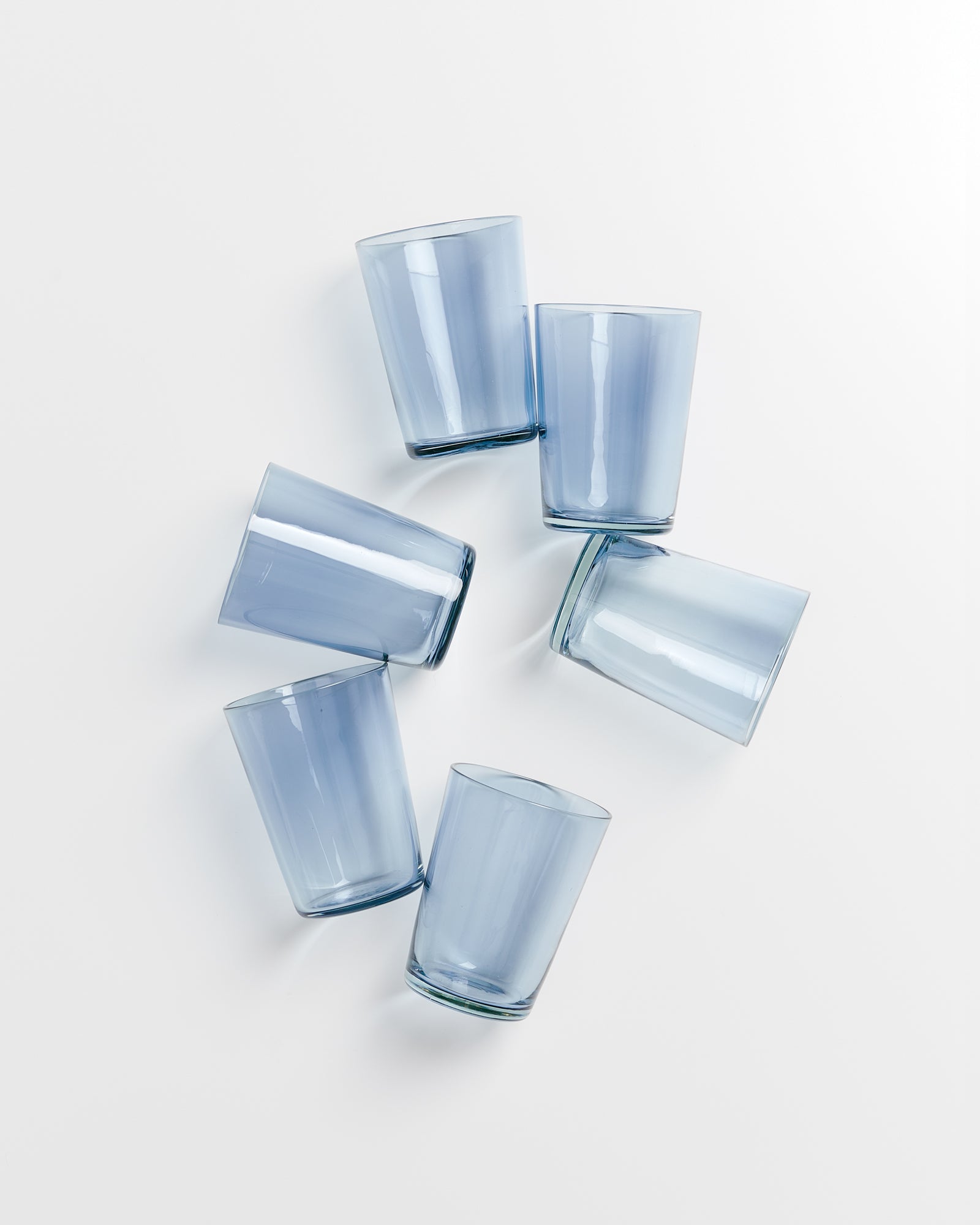 Fünf blaue Glasbecher liegen verstreut auf einer weißen Oberfläche.