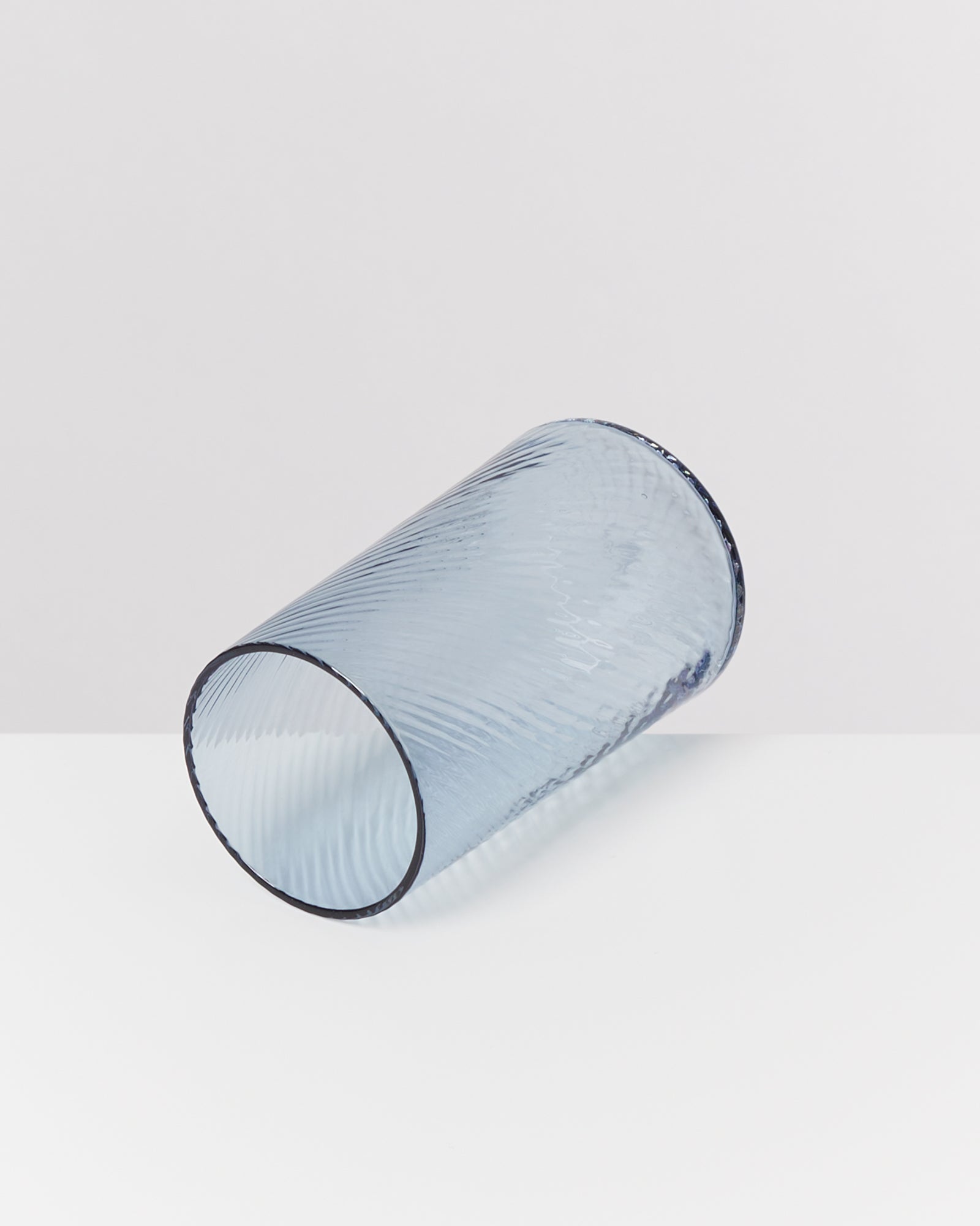 Ein graues, geriffeltes Trinkglas liegt seitlich auf einer weißen Oberfläche.