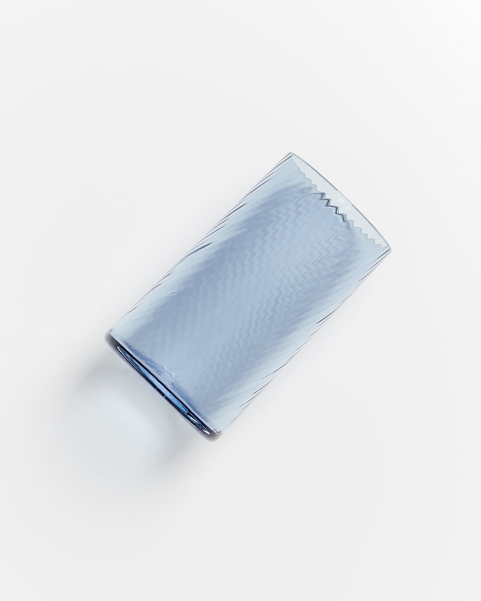 Ein leicht schräg liegendes, vertikal geriffeltes blaues Glas auf weißem Hintergrund.