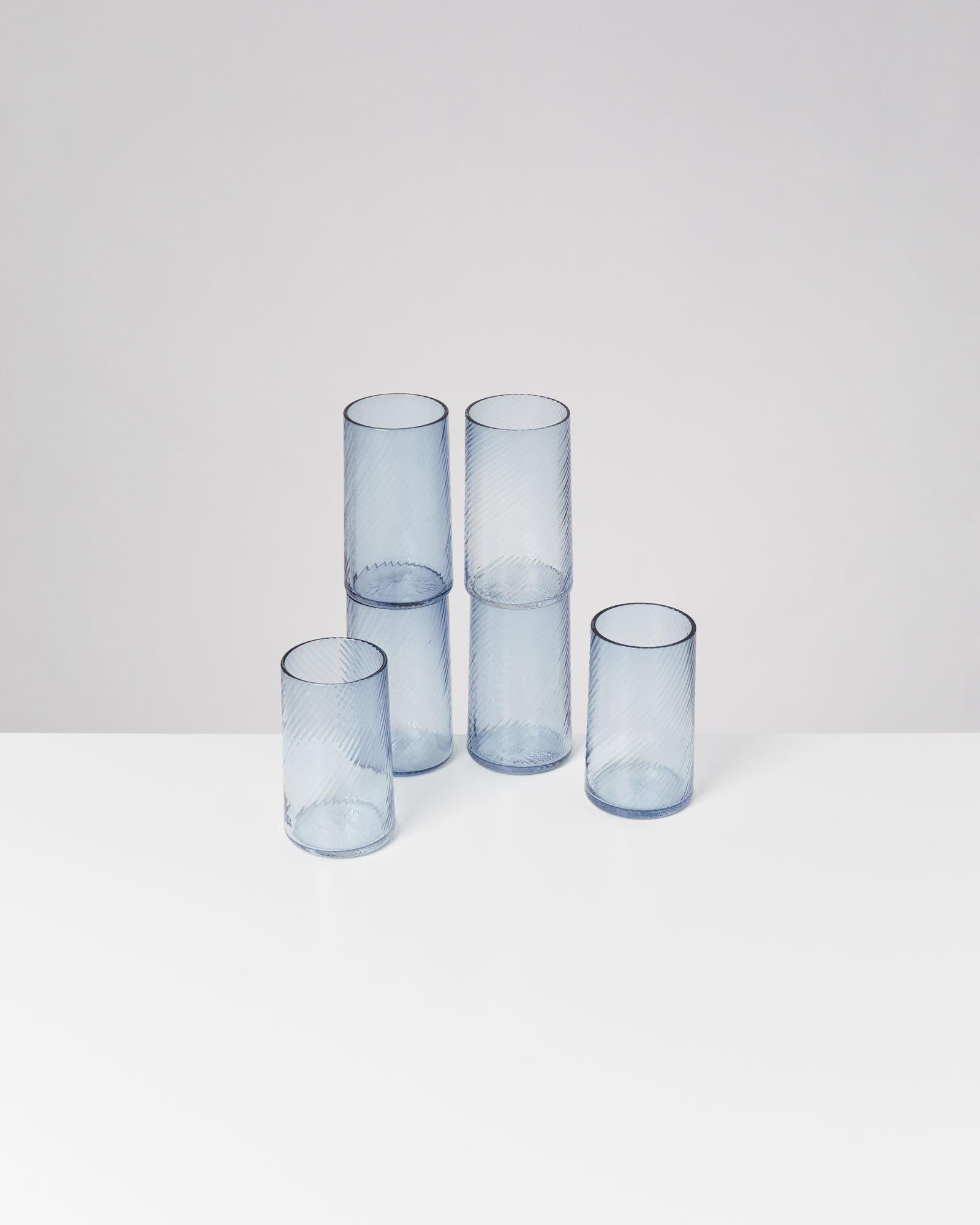 Fünf blaue, durchsichtige Gläser mit Rillenmuster stehen auf einem weißen Untergrund.