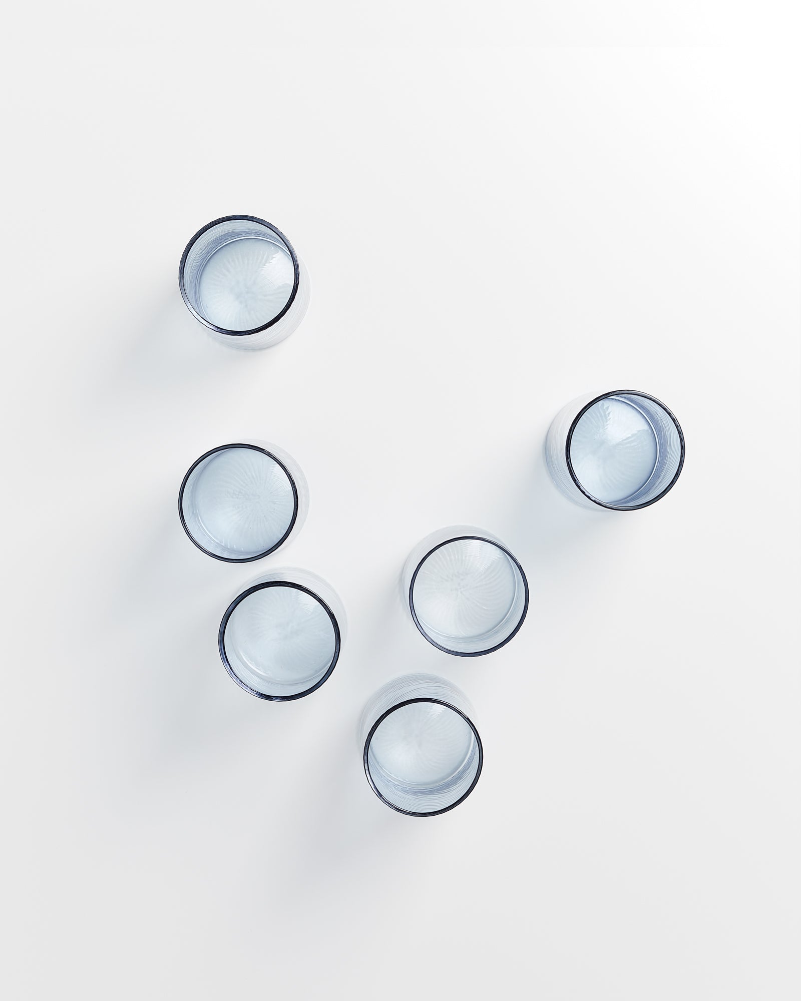 Fünf leere Wassergläser stehen in einem V auf einer weißen Oberfläche, von oben betrachtet.