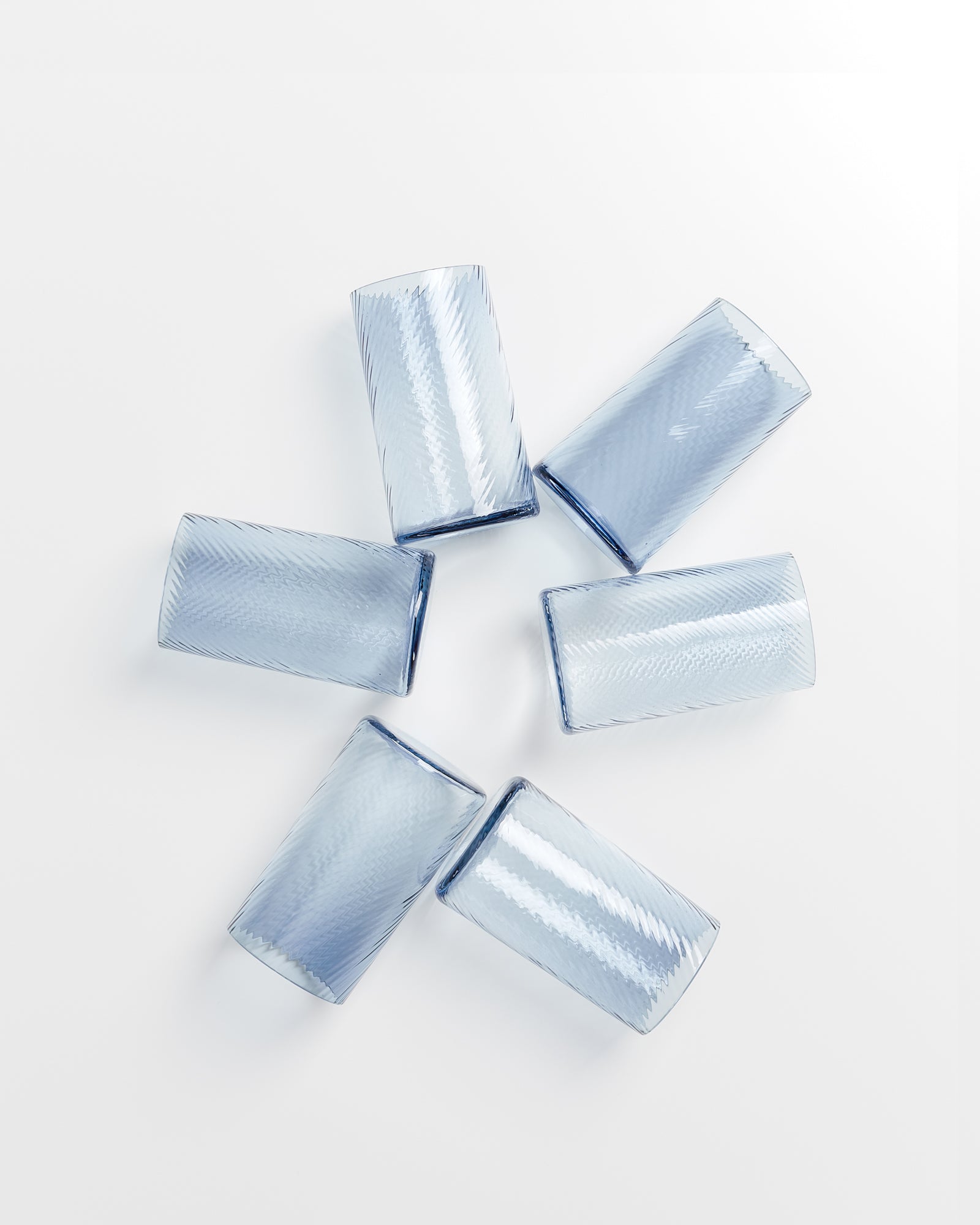 Sechs blaue Gläser liegen in einem Kreis auf einem weißen Hintergrund.