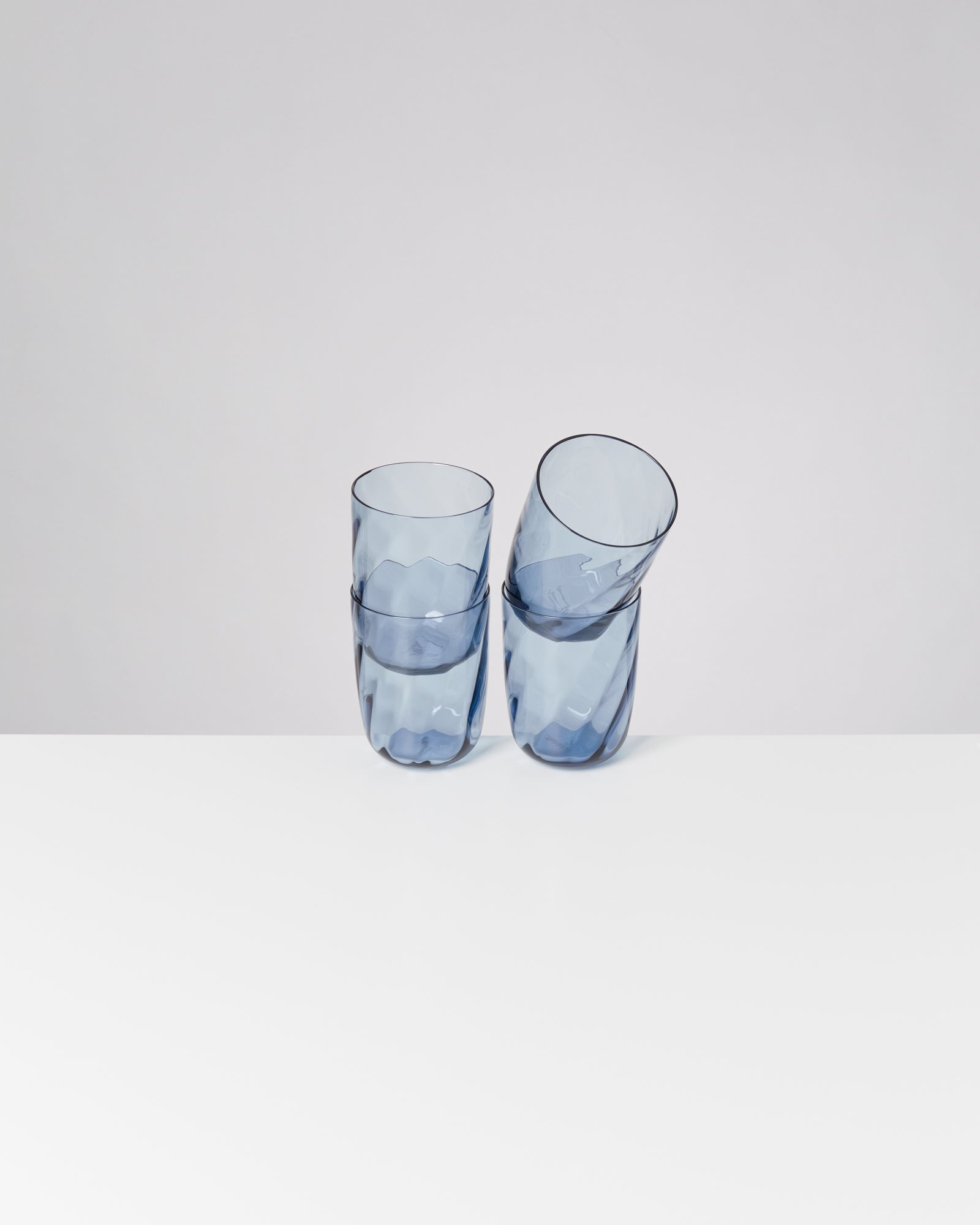 Zwei blaue, ineinander gestellte Gläser auf einem weißen Tisch vor neutralem Hintergrund.