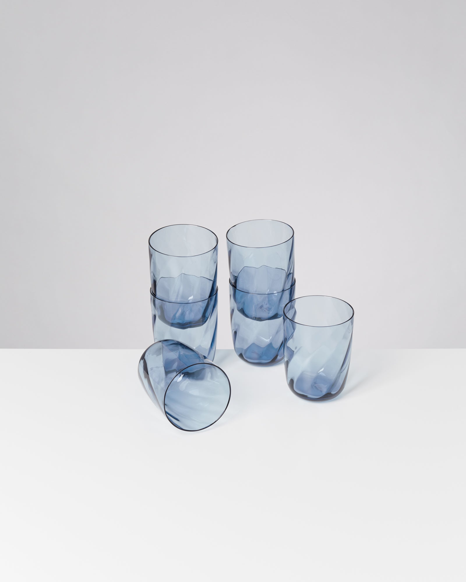 Fünf blaue, gestapelte Trinkgläser auf weißem Hintergrund, eins liegt seitlich.