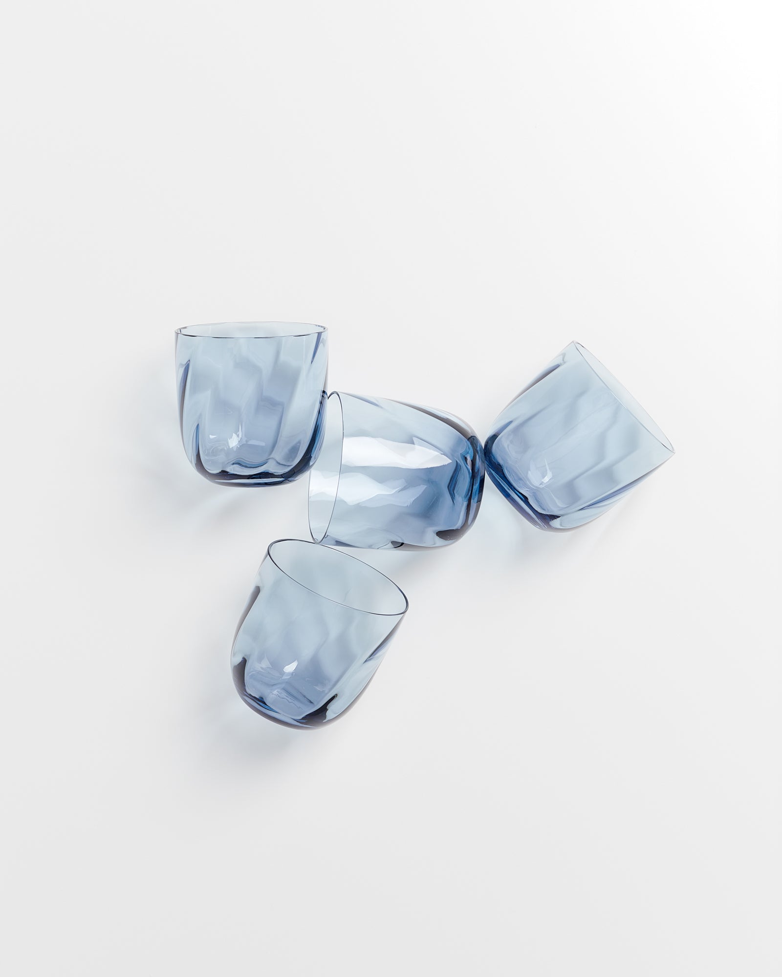 Vier blaue Gläser mit welliger Textur liegen auf einer weißen Oberfläche.