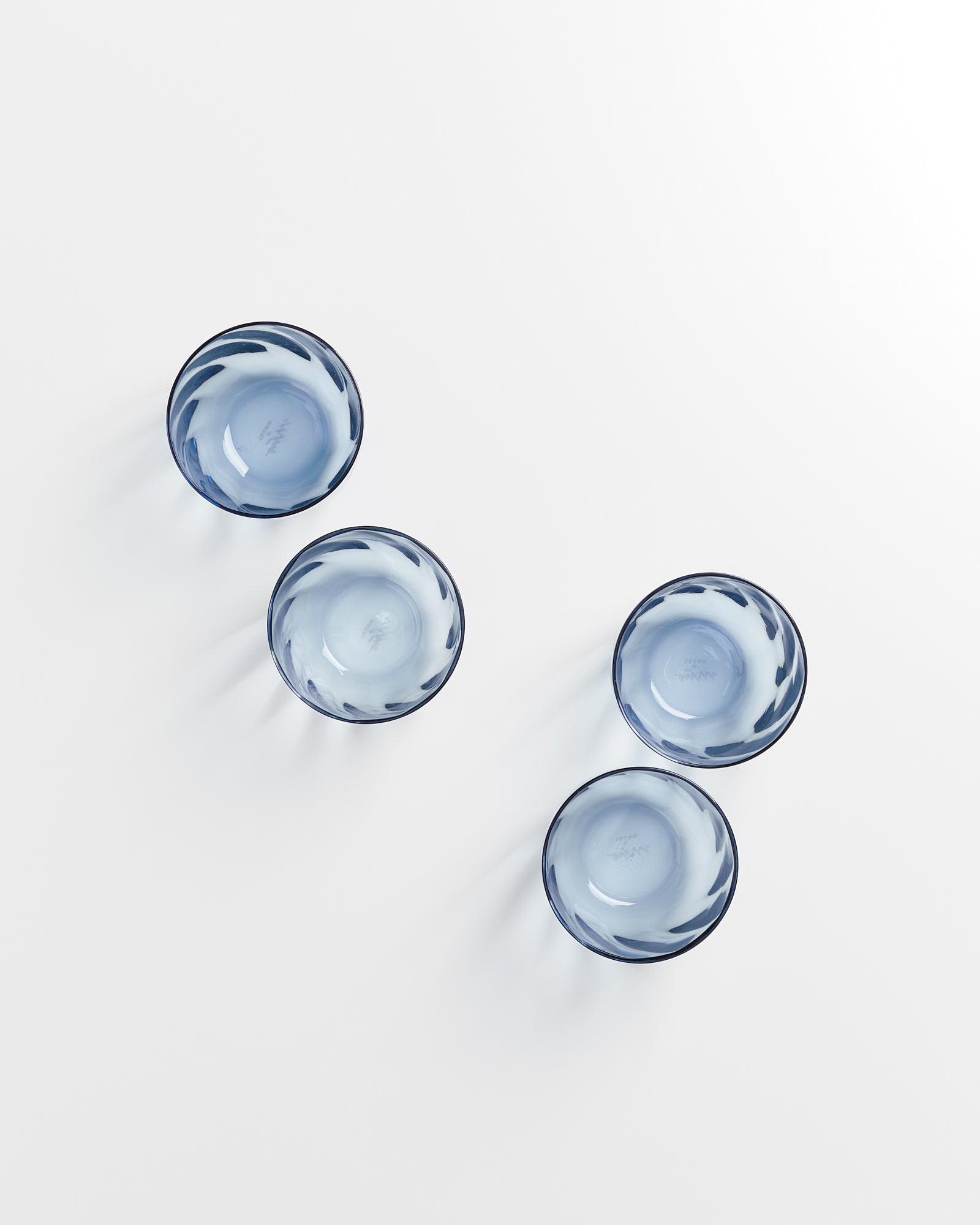 Vier blaue Glasschalen mit einem hellen Muster auf einem weißen Hintergrund.