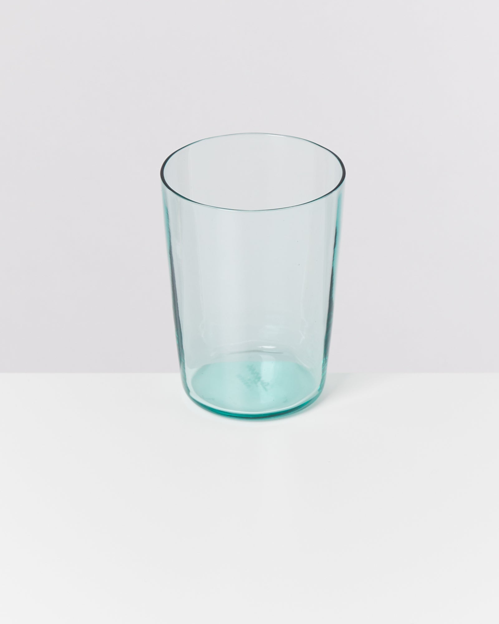 Ein klares Glas steht auf einer weißen Oberfläche vor einem hellgrauen Hintergrund.