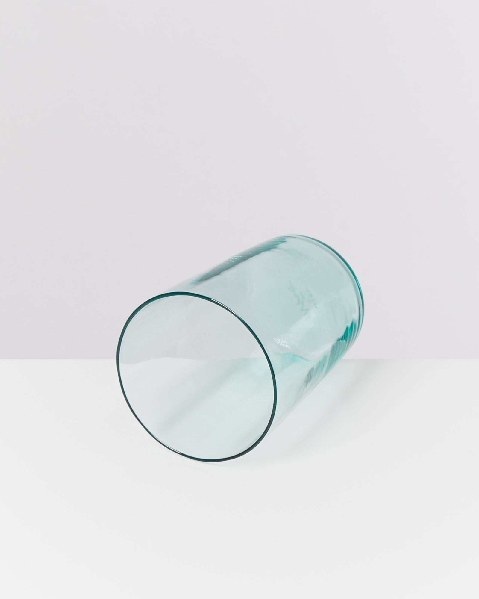Ein transparentes Glas liegt seitlich auf einer weißen Oberfläche vor einem hellgrauen Hintergrund.