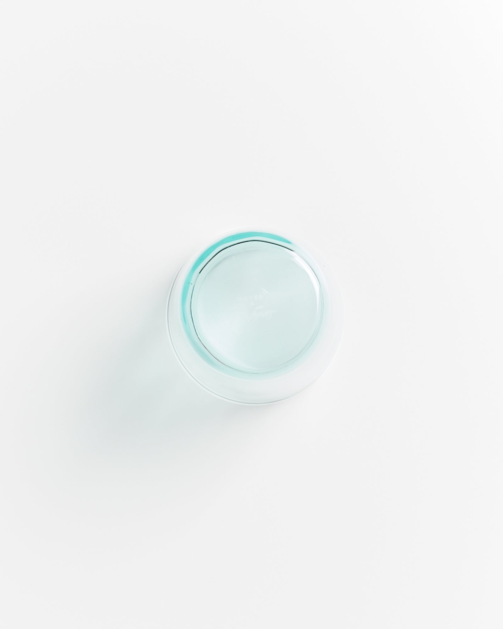 Gläserne Schale mit türkisfarbener Flüssigkeit, auf weißem Hintergrund von oben fotografiert.