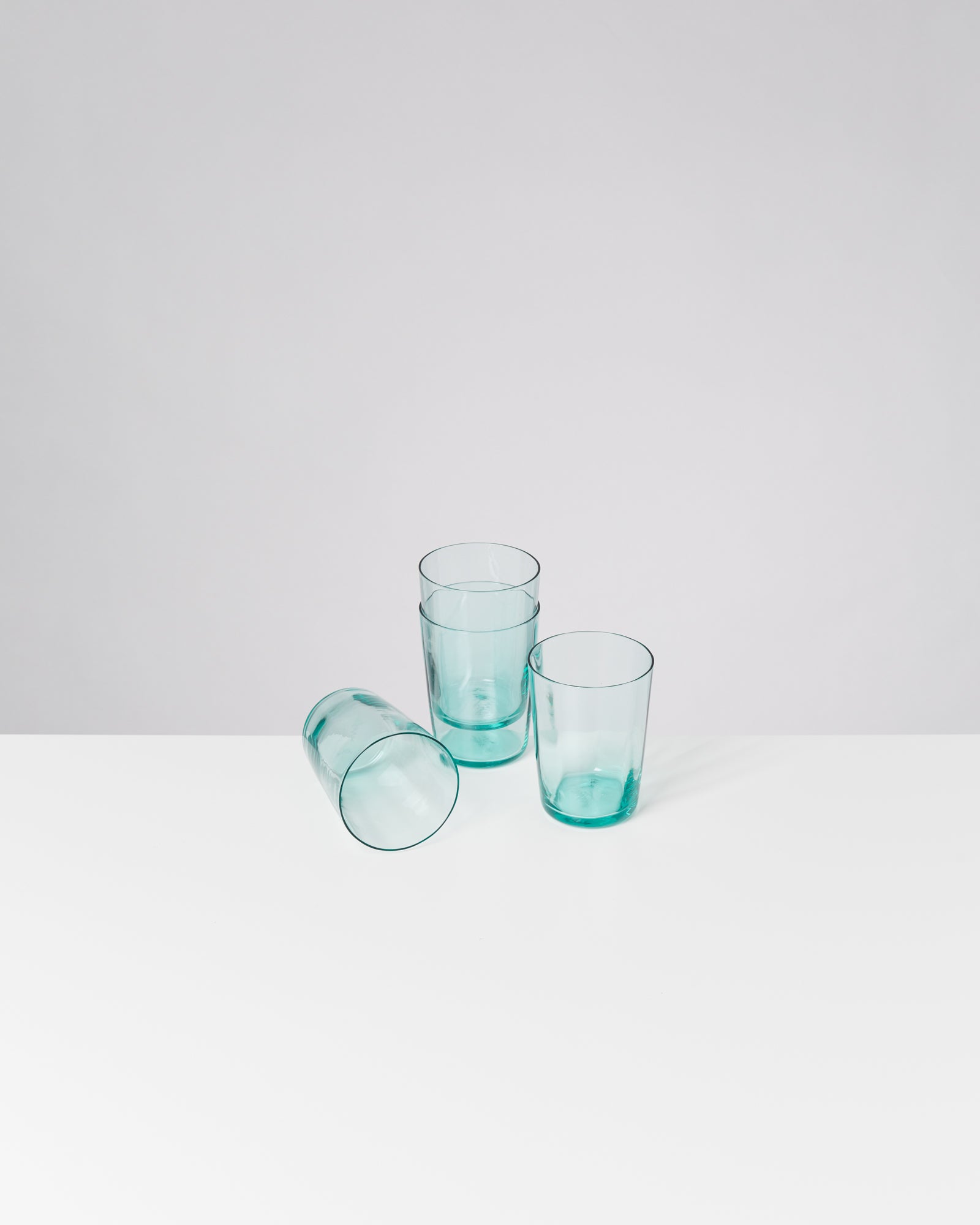 Drei leere, grüne Gläser auf einem weißen Tisch, eines liegt seitlich.