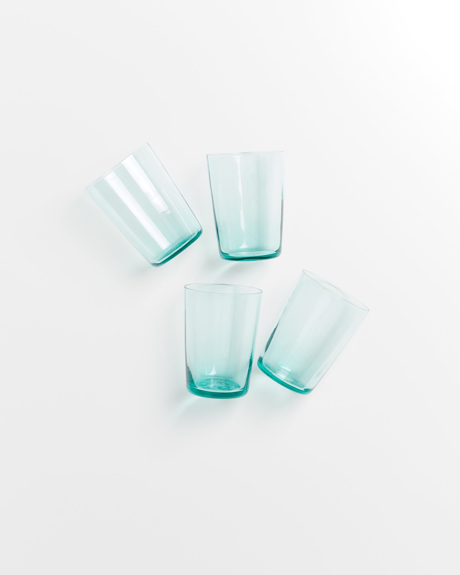 Vier grüne Gläser auf weißem Hintergrund, zwei davon leicht gekippt.