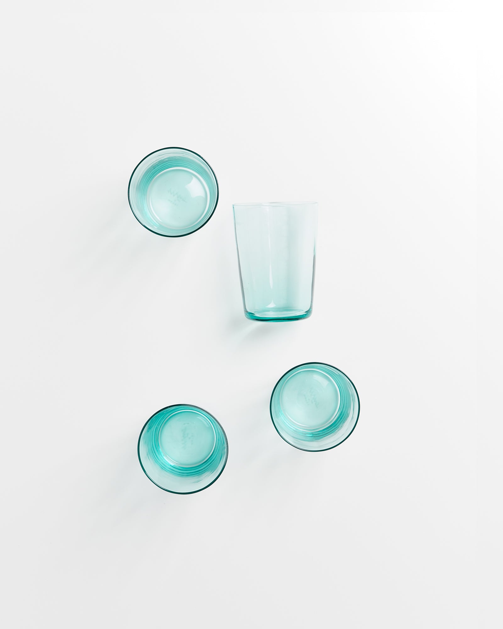 Vier türkisfarbene Gläser, drei umgedreht, eins aufrecht, auf weißem Hintergrund angeordnet.