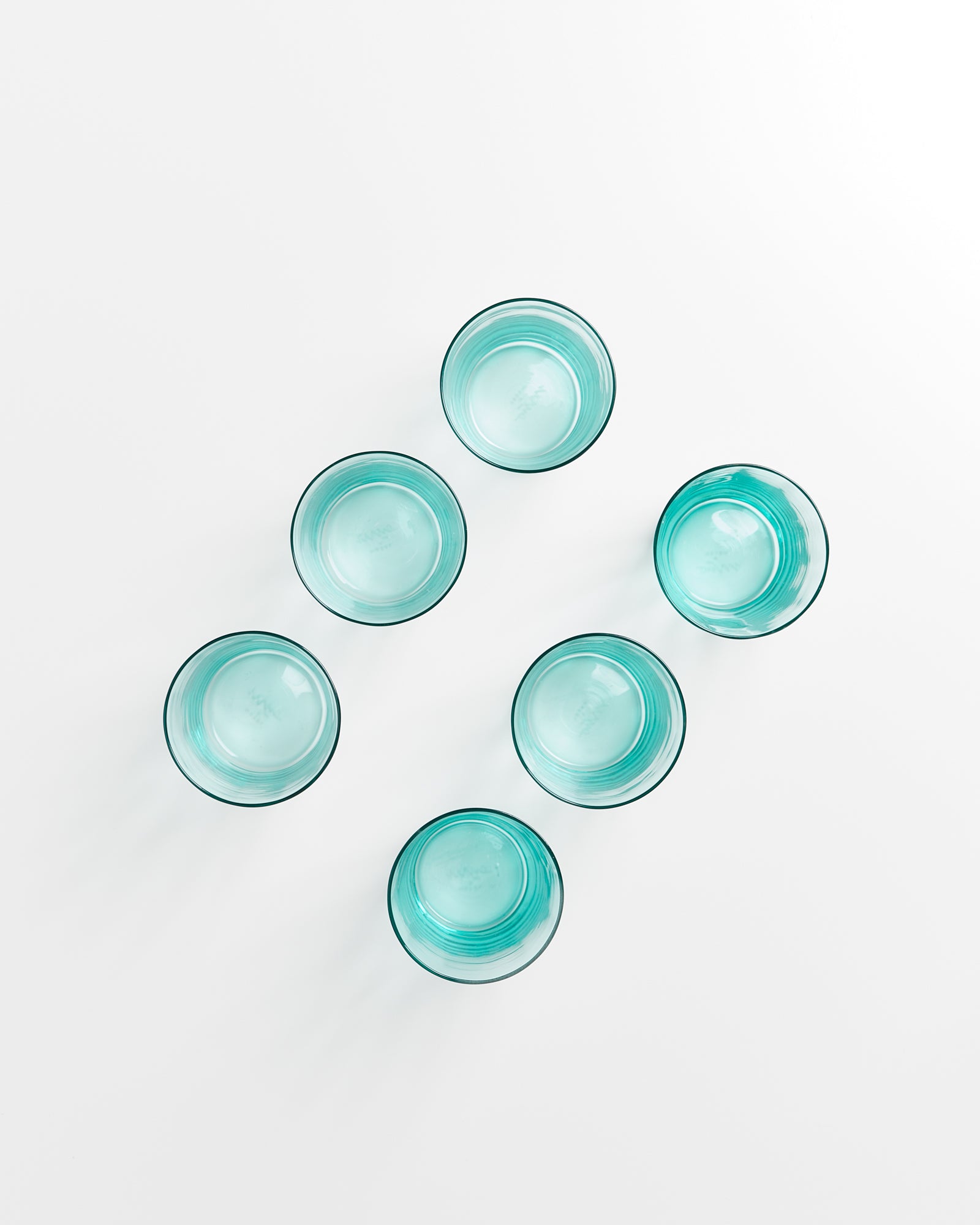 Sechs blaue Gläser sind in einem diagonalen Muster auf einem weißen Hintergrund angeordnet.