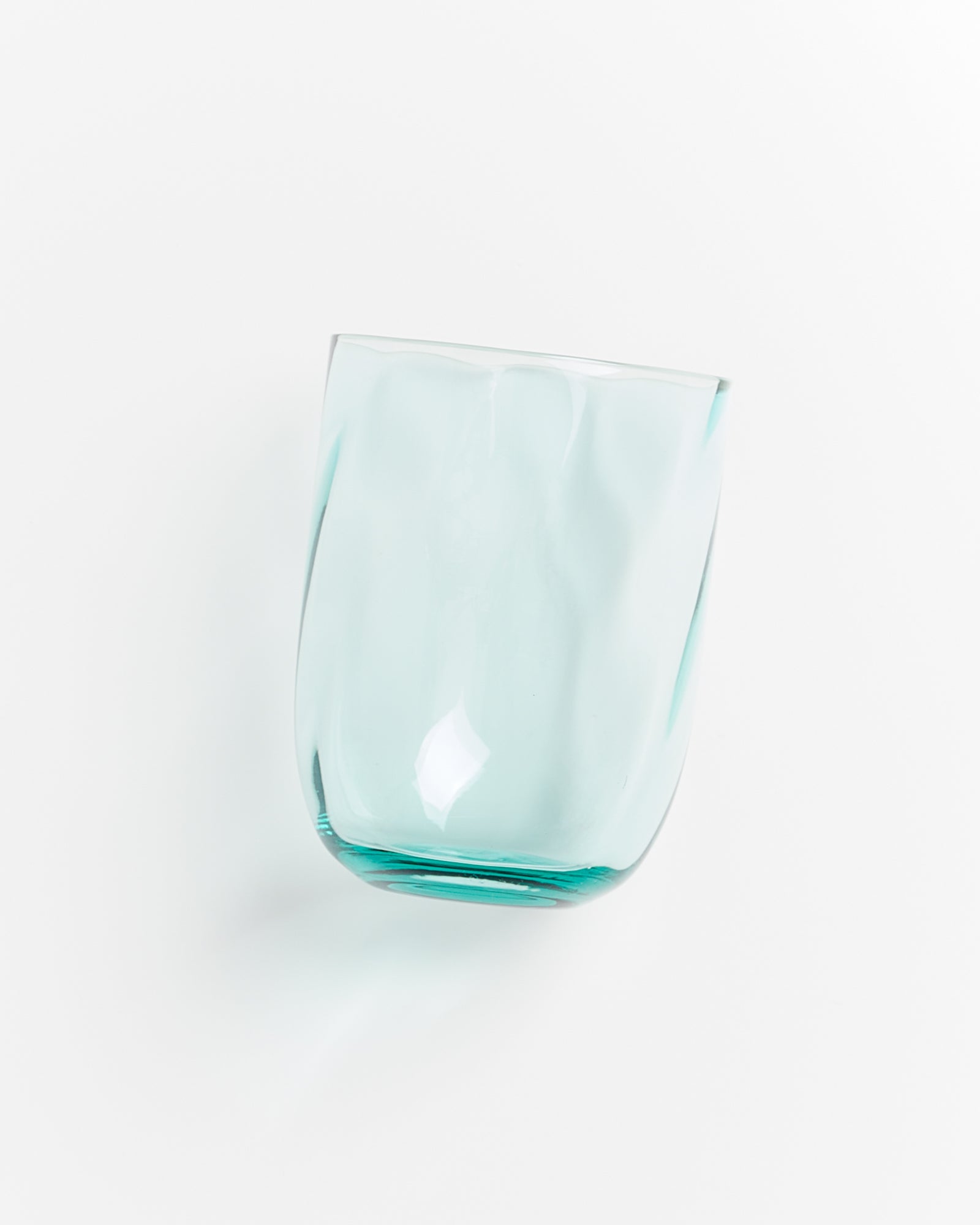 Ein transparentes, leicht bläuliches Trinkglas mit unregelmäßiger Oberfläche auf weißem Hintergrund.