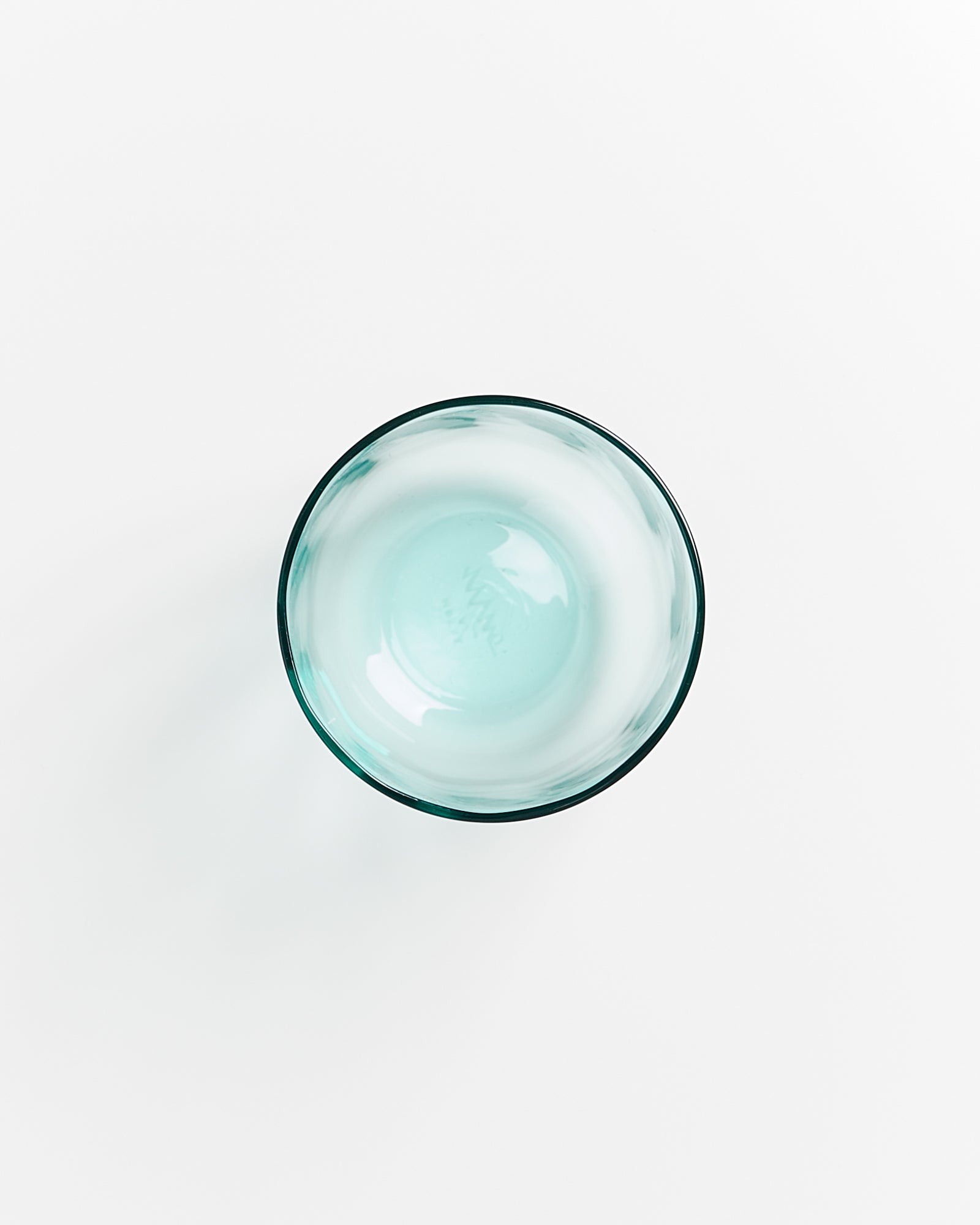 Transparente, hellblaue Glaskugel aus Glas, auf einer weißen Oberfläche von oben aufgenommen.