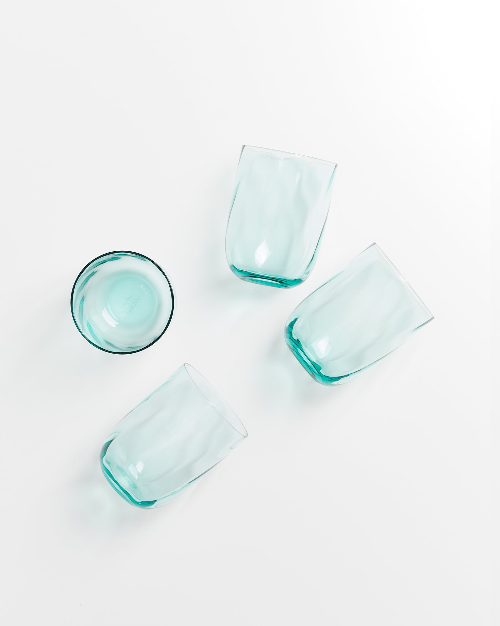 Vier leichte, bläulich schimmernde Trinkgläser liegen auf einem weißen Hintergrund, eines stehend und drei liegend.