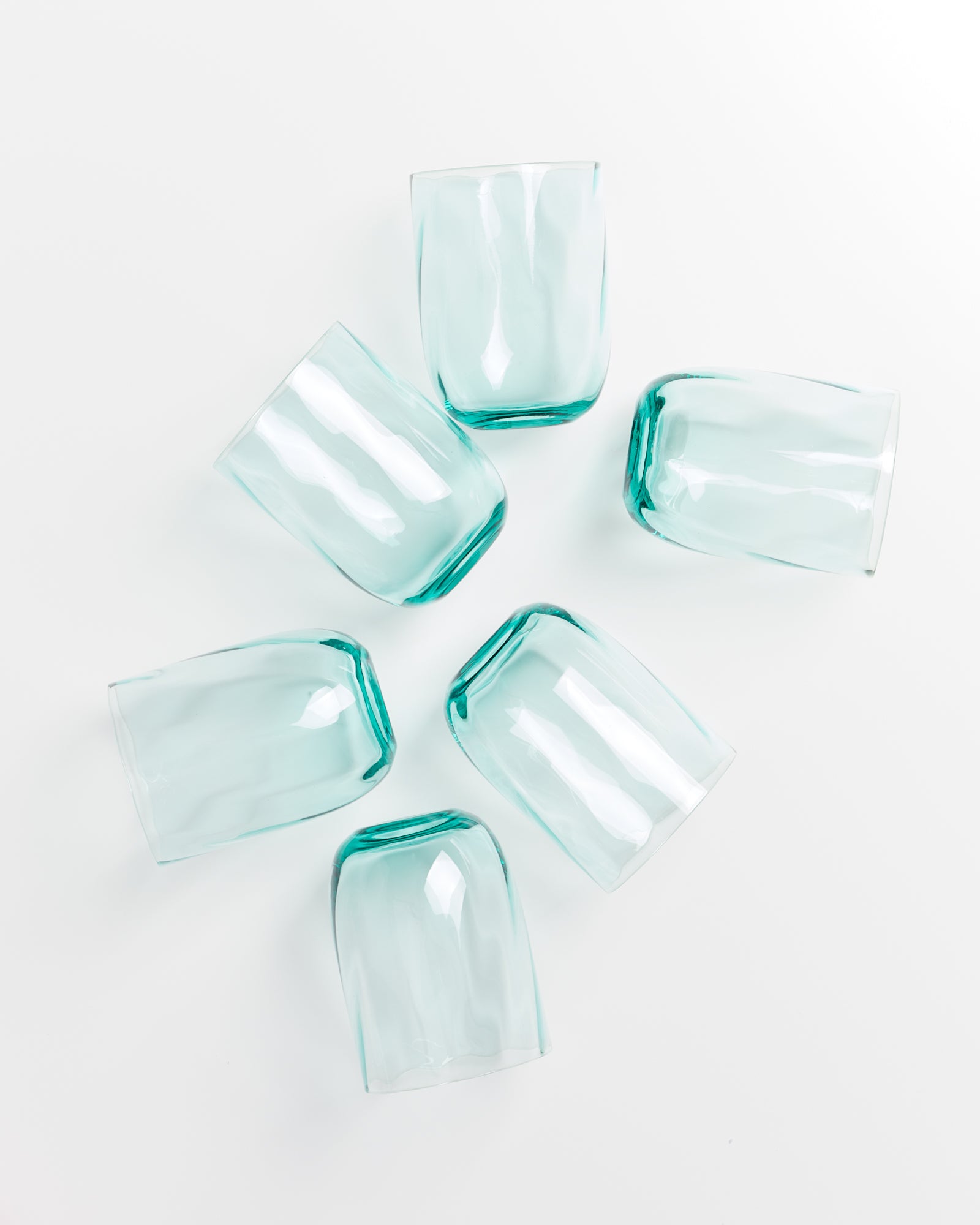 Sechs türkisfarbene Gläser liegen in einem Kreis auf einer weißen Oberfläche.