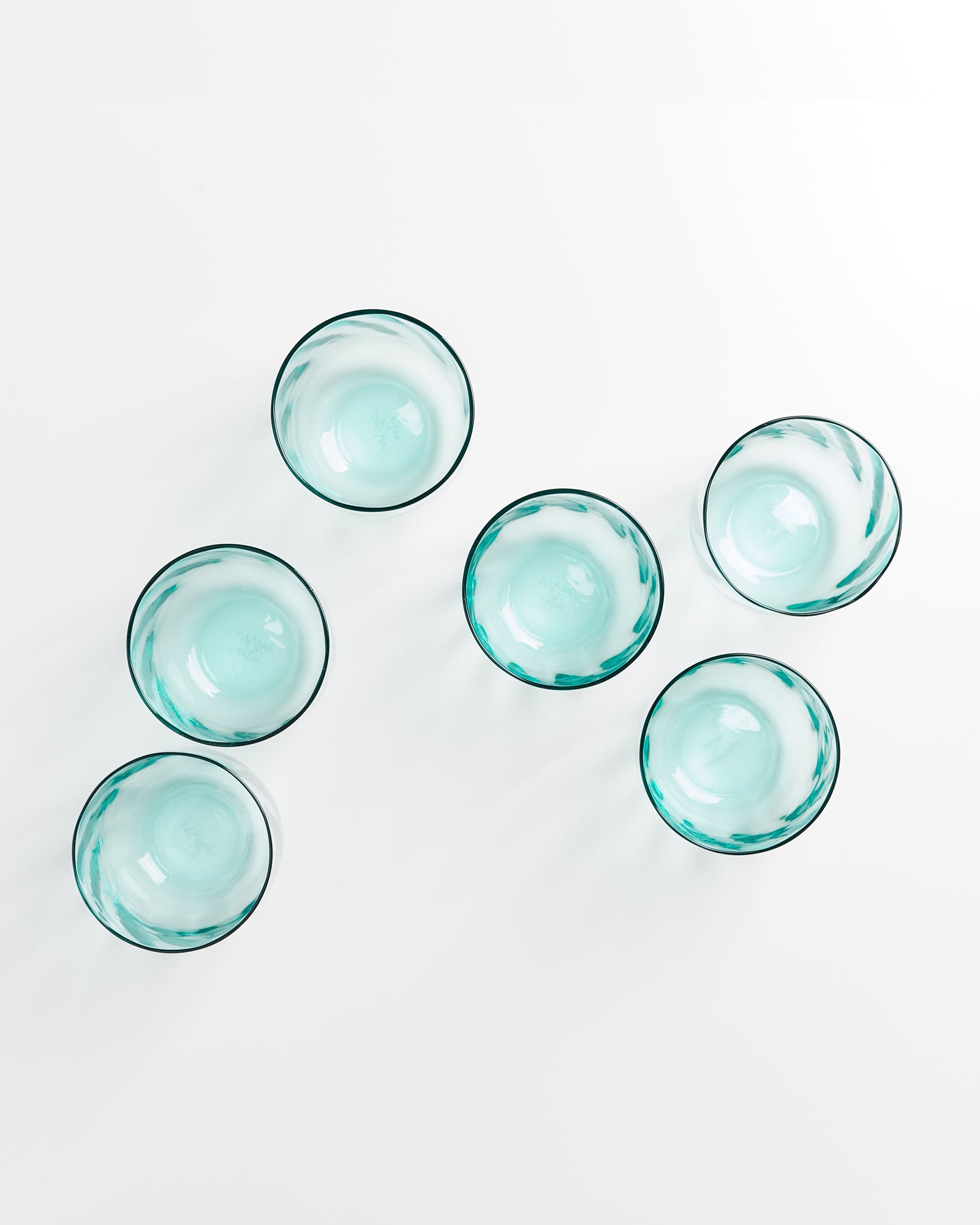 Sechs türkisfarbene Schalen sind auf einer weißen Oberfläche geometrisch angeordnet.