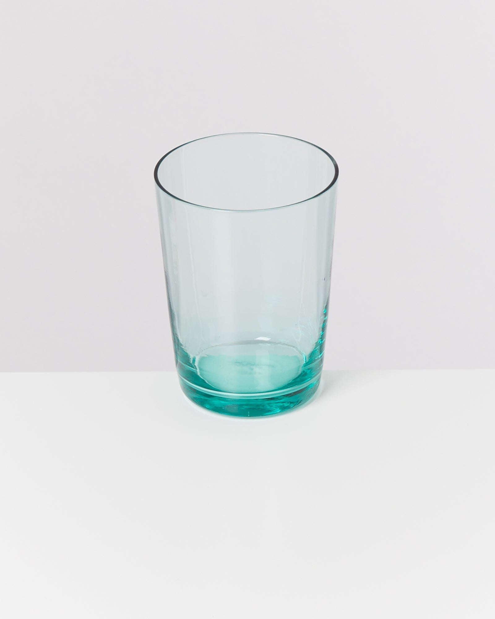 Ein leeres, hellblaues Trinkglas steht auf einer weißen Oberfläche.