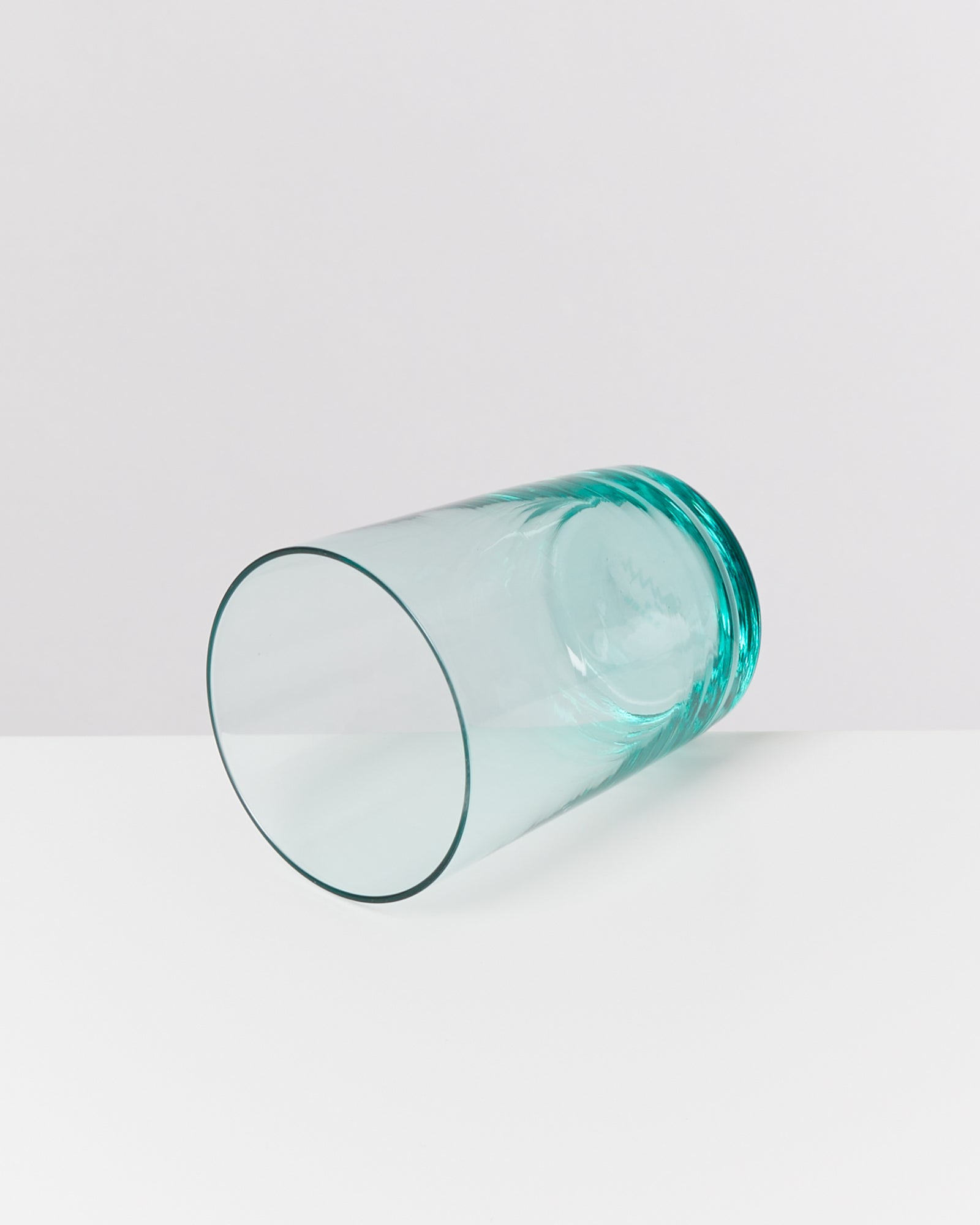 Ein umgekippter, durchsichtiger grüner Glasbecher liegt auf einer weißen Oberfläche.
