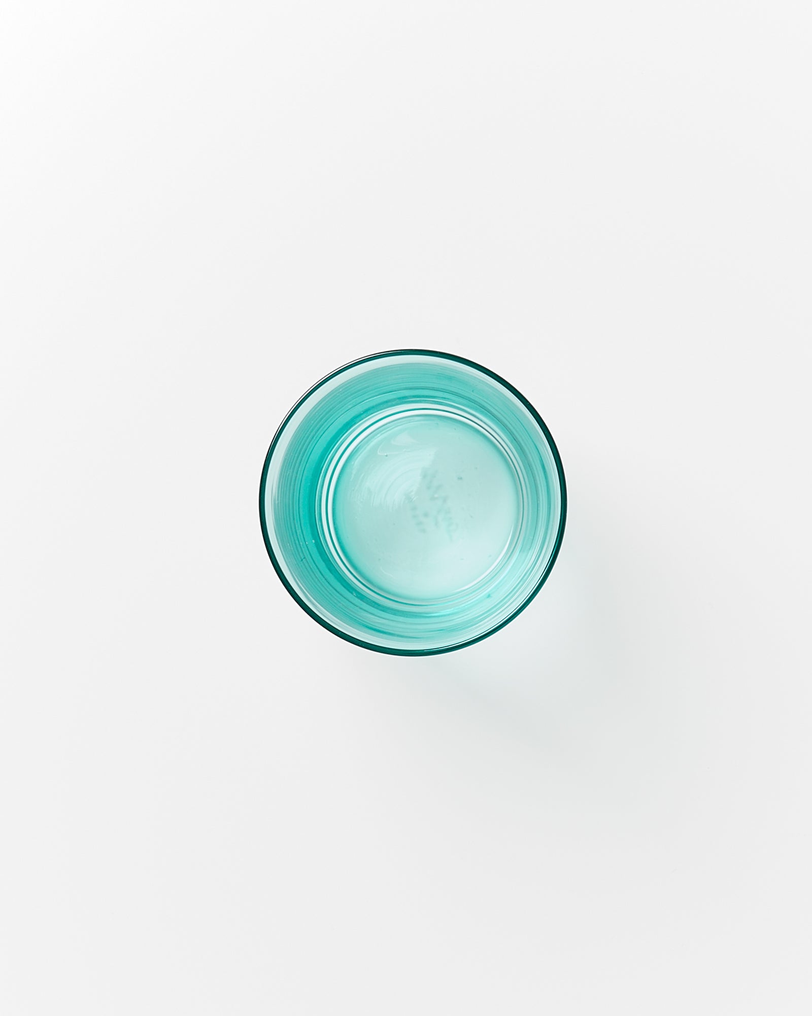 Ein Glas mit blauem Wasser steht auf einem weißen Hintergrund, von oben betrachtet.