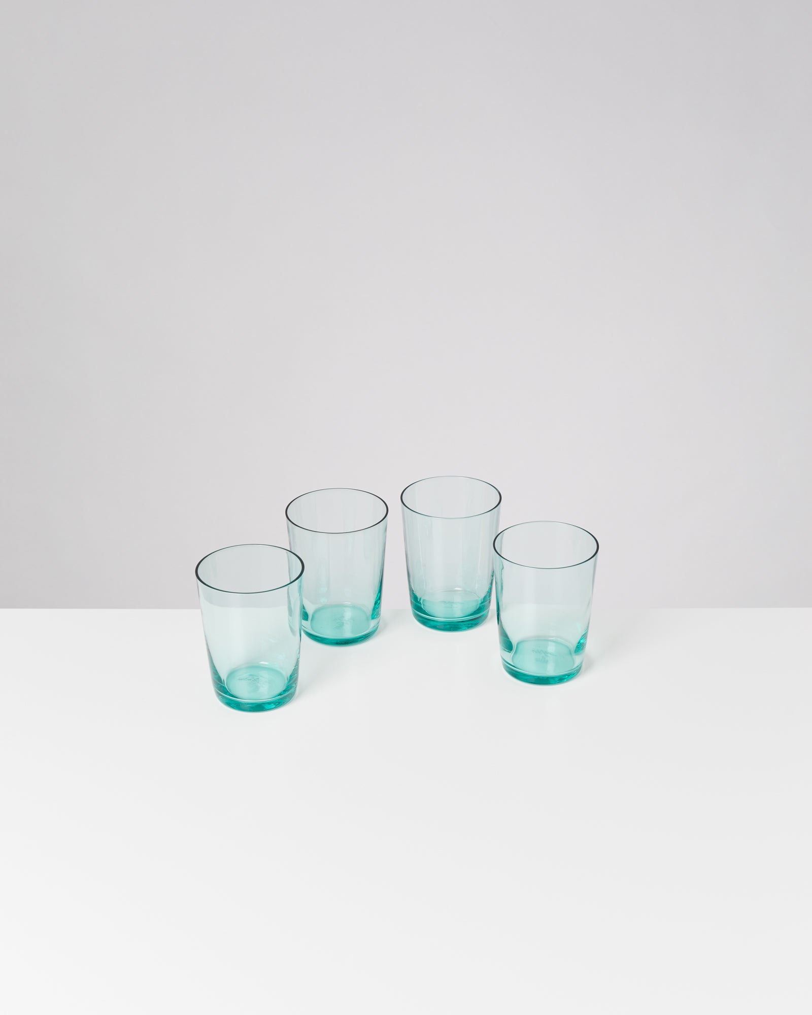 Vier hellblaue Gläser stehen auf einem weißen Tisch vor einem neutralen Hintergrund.