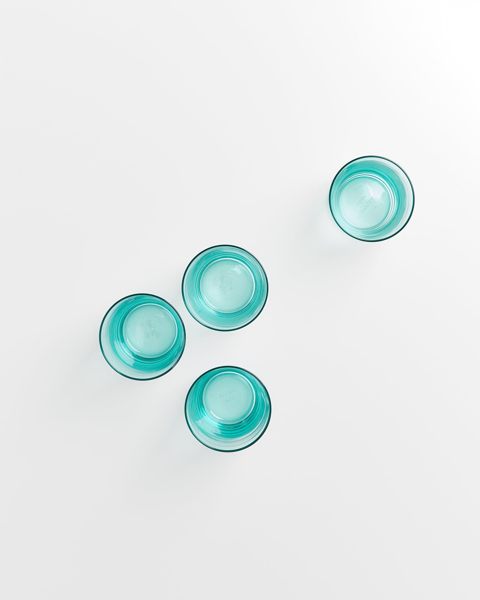 Vier türkise Gläser auf weißem Hintergrund in diagonalem Muster angeordnet.