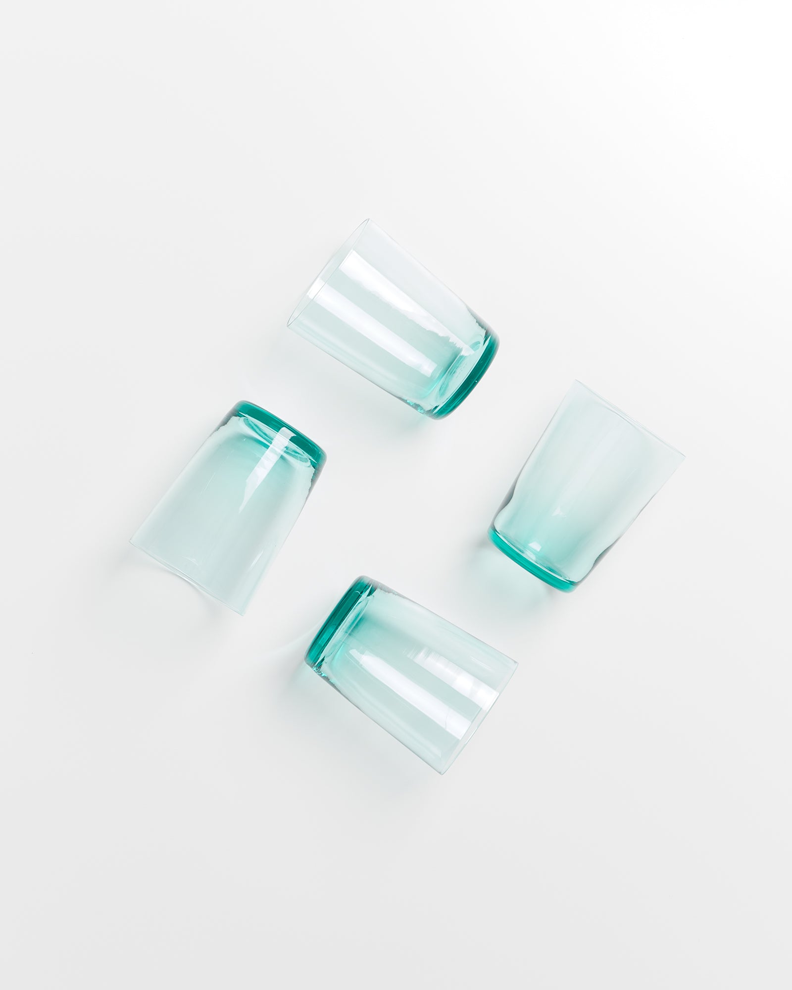 Vier grüne Gläser liegen in verschiedenen Winkeln auf einer weißen Oberfläche.