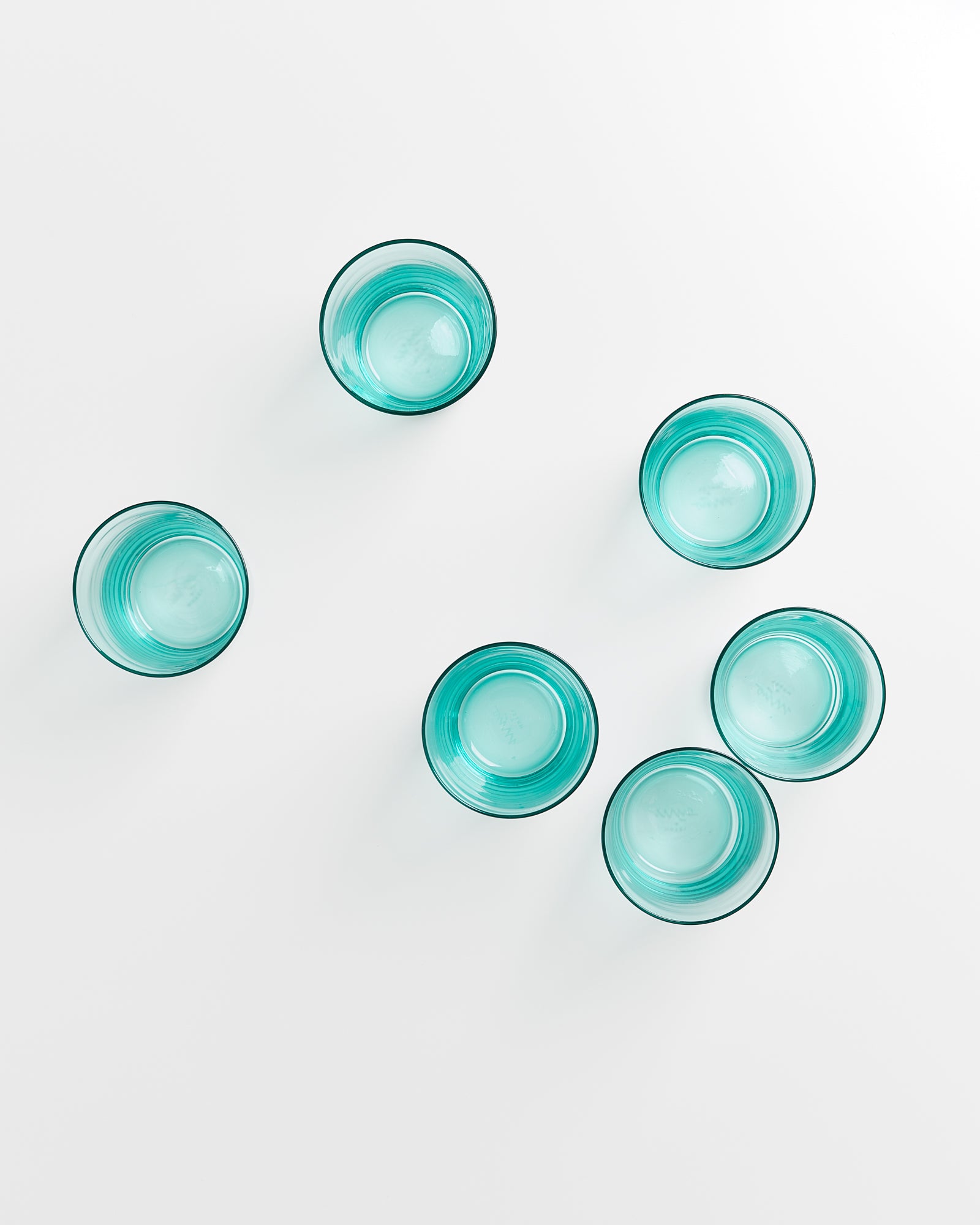 Sechs leere, türkisfarbene Gläser auf weißem Hintergrund, von oben betrachtet.