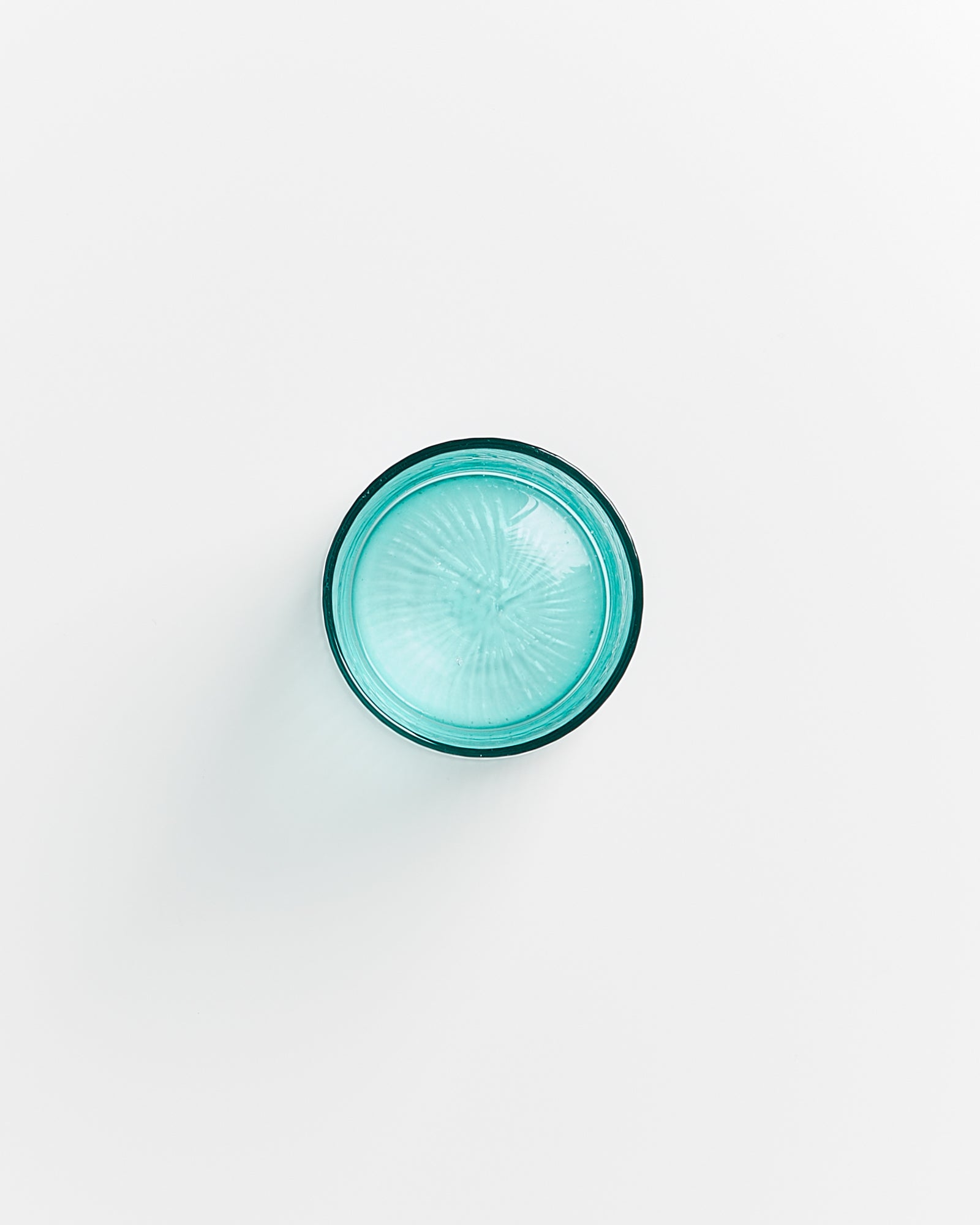 Ein klares, türkisfarbenes Trinkglas, von oben fotografiert, auf einem weißen Hintergrund.