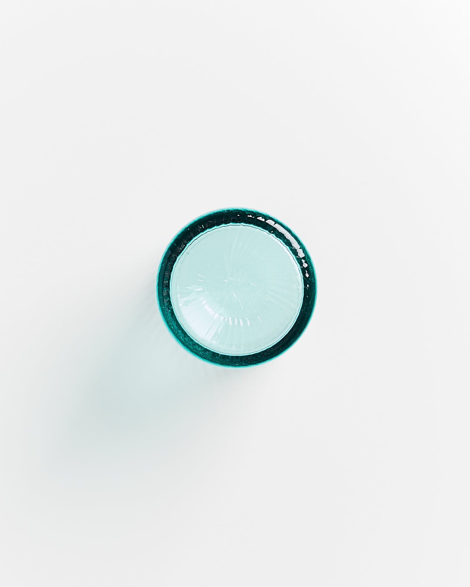 Kreisförmiges, türkisfarbenes Glasobjekt von oben betrachtet auf weißem Hintergrund.