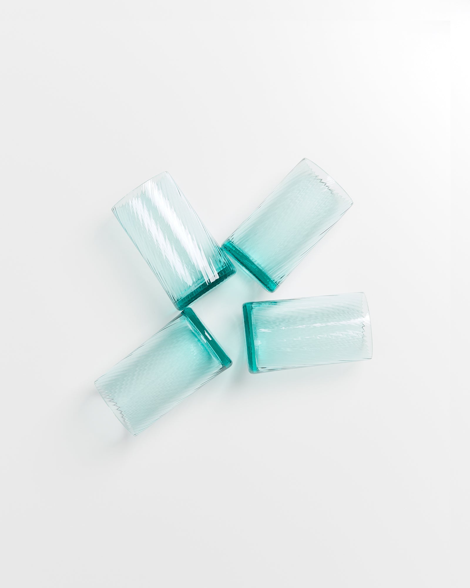 Vier türkisfarbene Gläser liegen in einer kreuzförmigen Anordnung auf weißem Hintergrund.