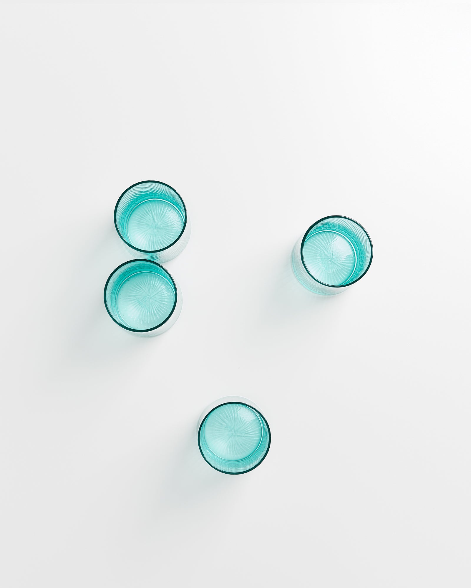 Vier türkisfarbene Gläser sind auf einer weißen Fläche arrangiert.