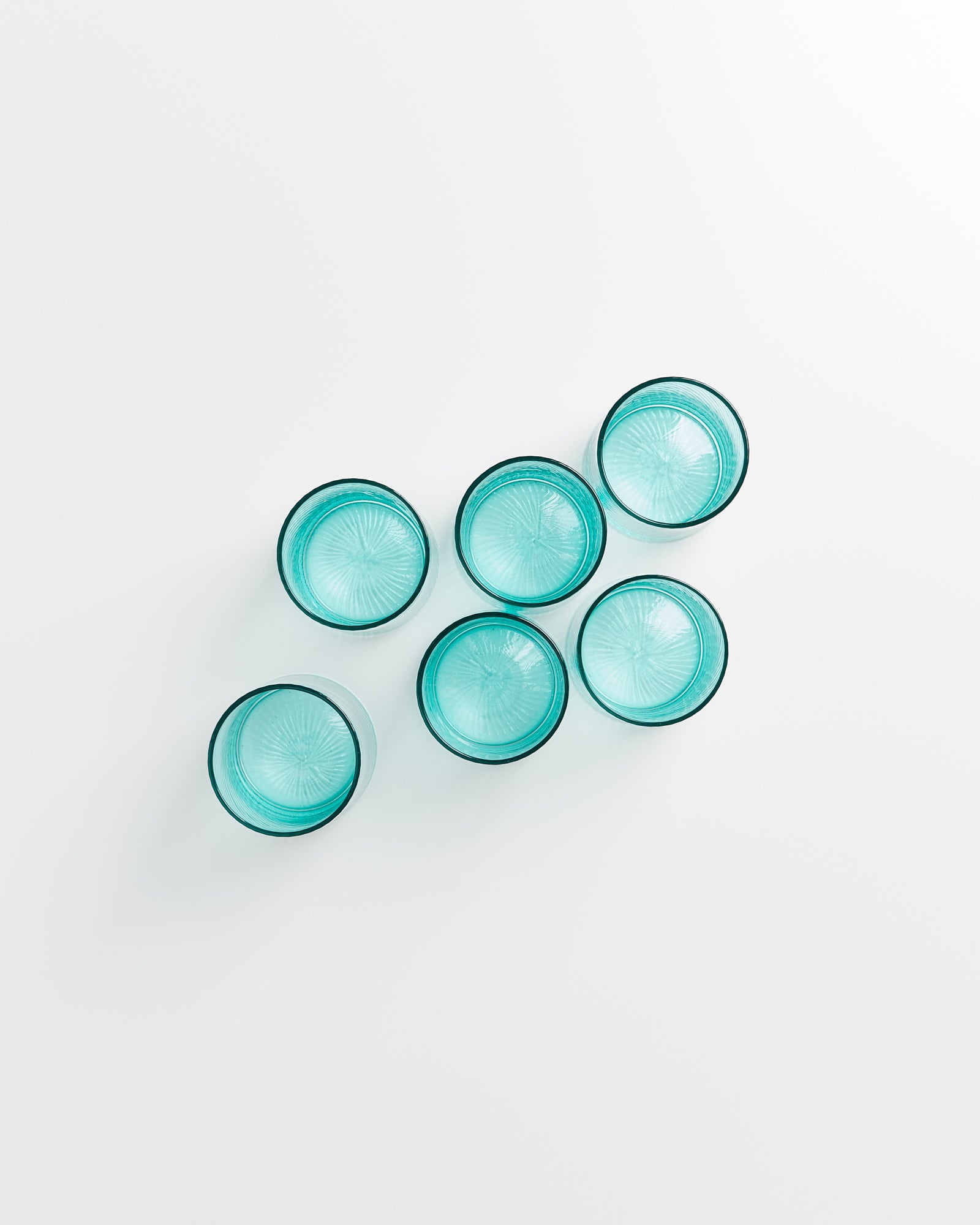 Sechs blaue Gläser in zwei Reihen auf einer weißen Oberfläche angeordnet.