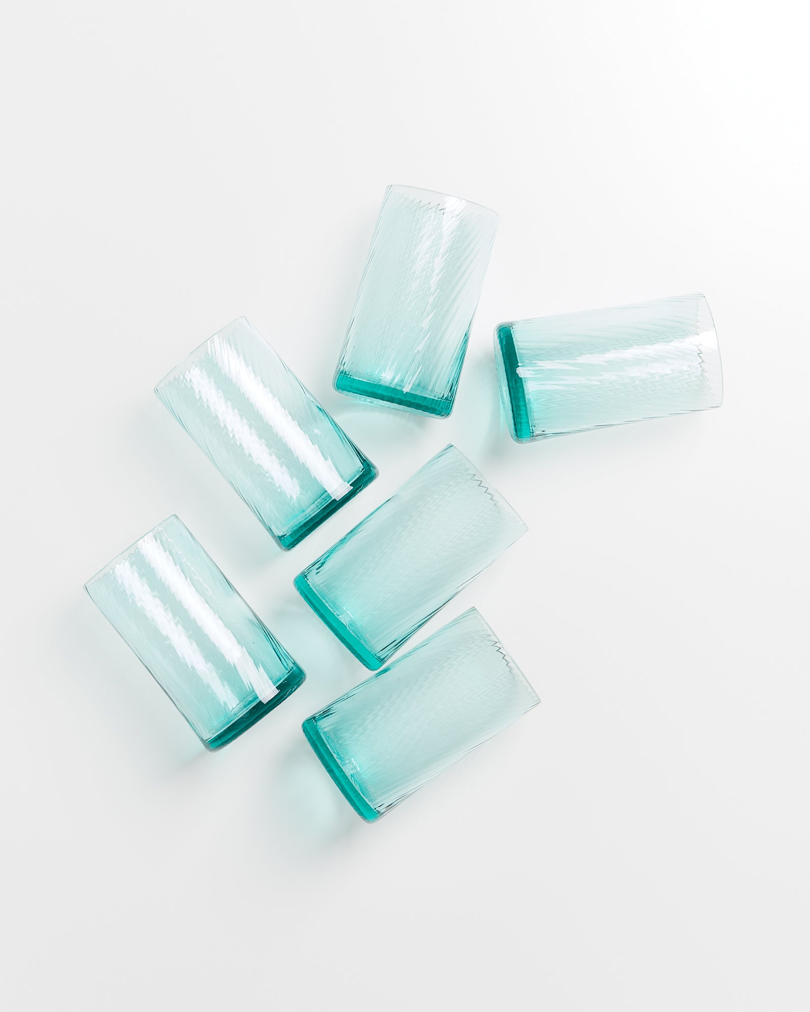 Sechs blaue Gläser liegen auf einem weißen Hintergrund verteilt.