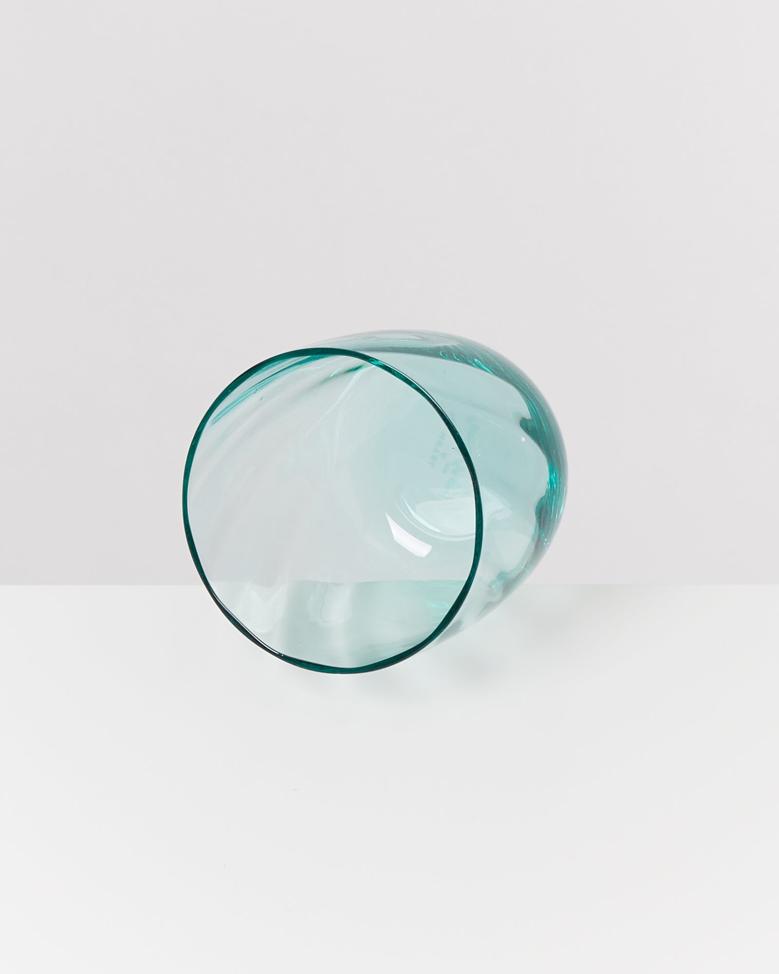 Ein transparentes, türkisfarbenes Glas liegt auf der Seite auf einer weißen Oberfläche.