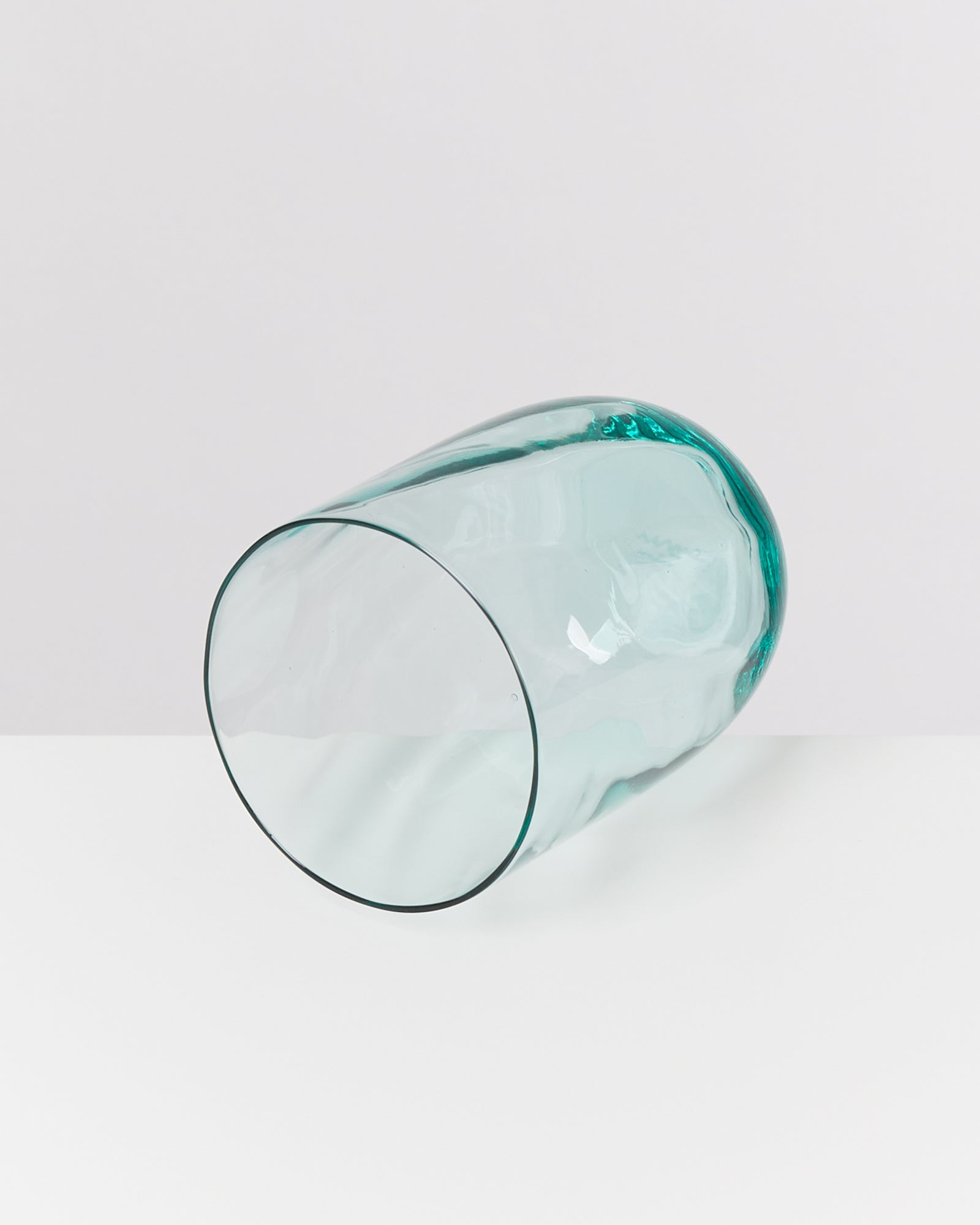 Grünes Glasgefäß liegt horizontal auf einer weißen Fläche.