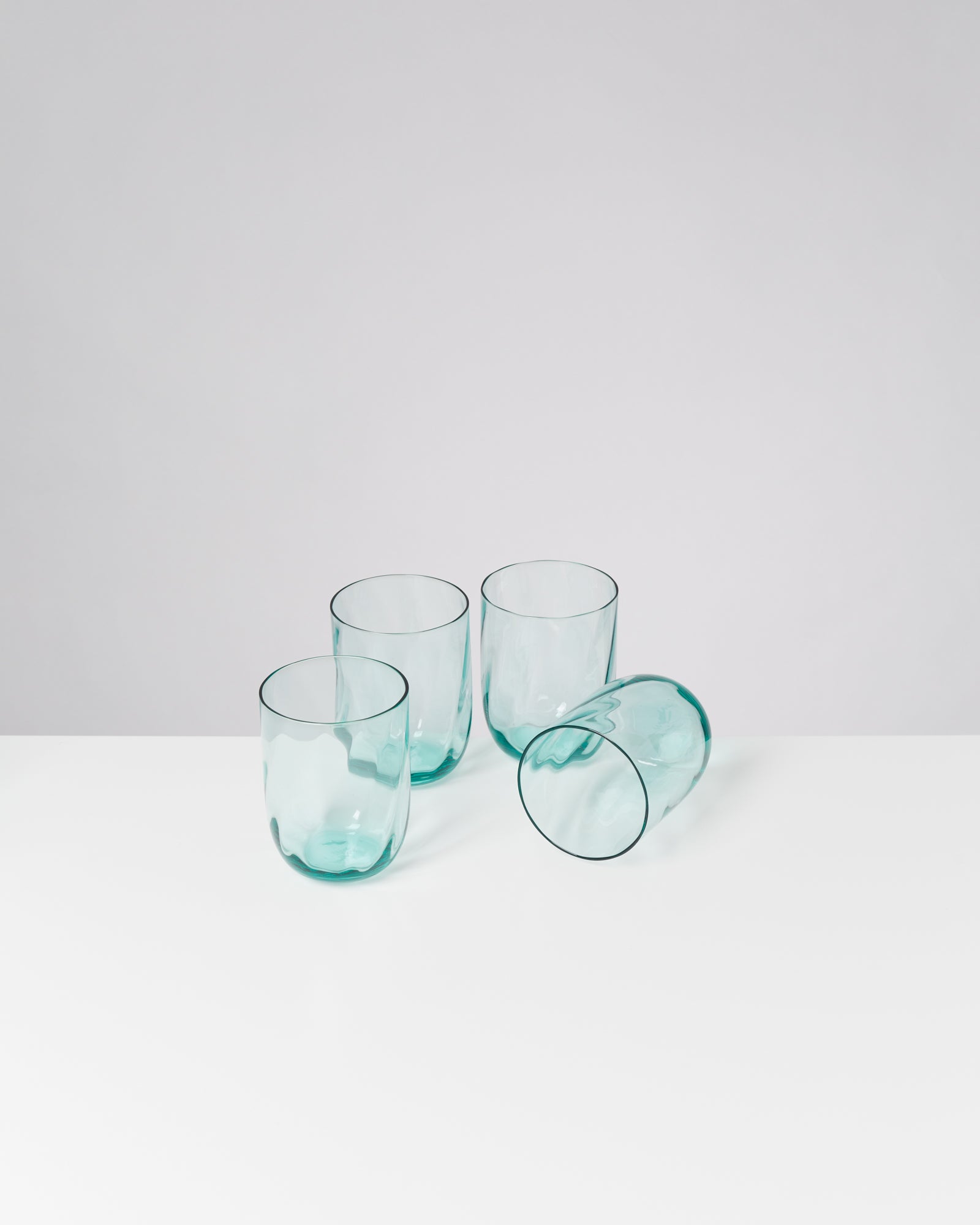 Vier türkisfarbene Trinkgläser auf einem weißen Tisch, eines davon liegt auf der Seite.